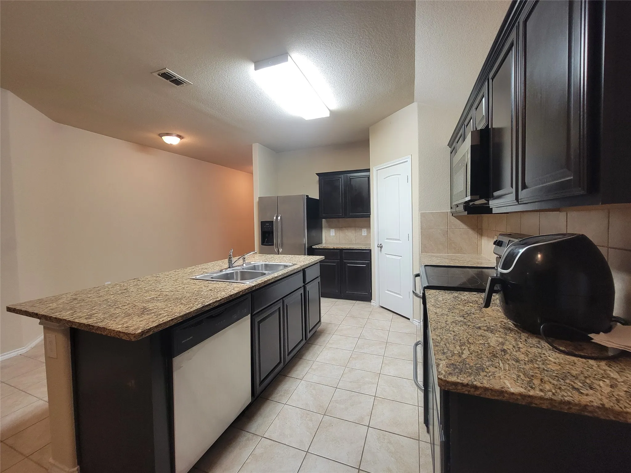 Kitchen featuring a large island with sink, dark cabinetry, and light-toned countertops