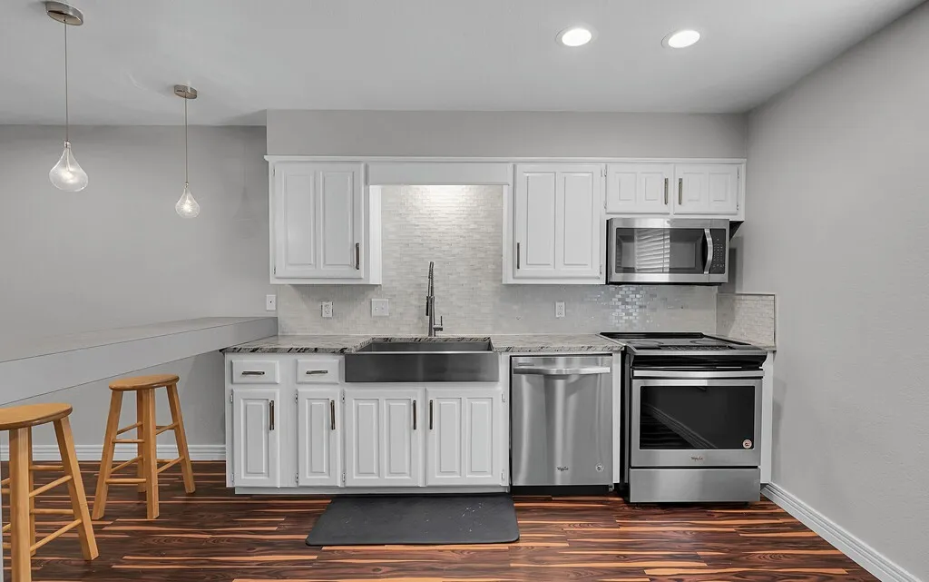 Modern kitchen featuring white cabinetry, stainless steel appliances, a farmhouse sink, and wood-finish flooring