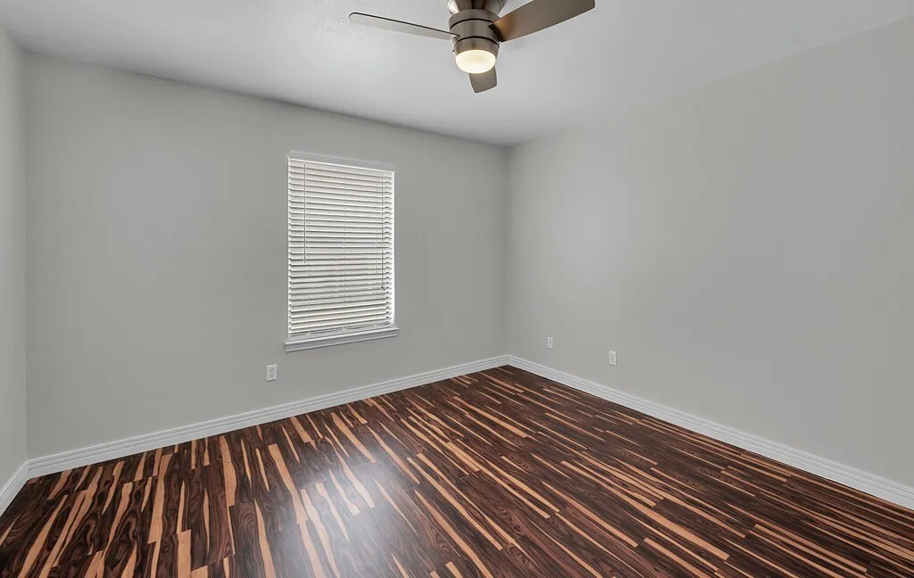 Wood-finish flooring, light gray wall paint, window with blinds, and ceiling fan with integrated lighting