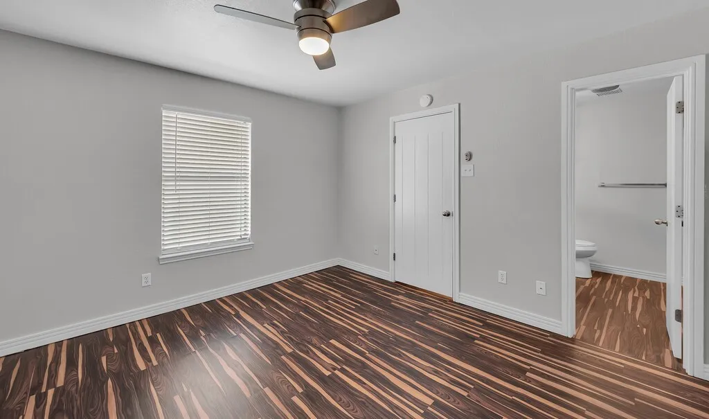 Wood-finish flooring, ceiling fan with integrated lighting, window with horizontal blinds, and white interior doors