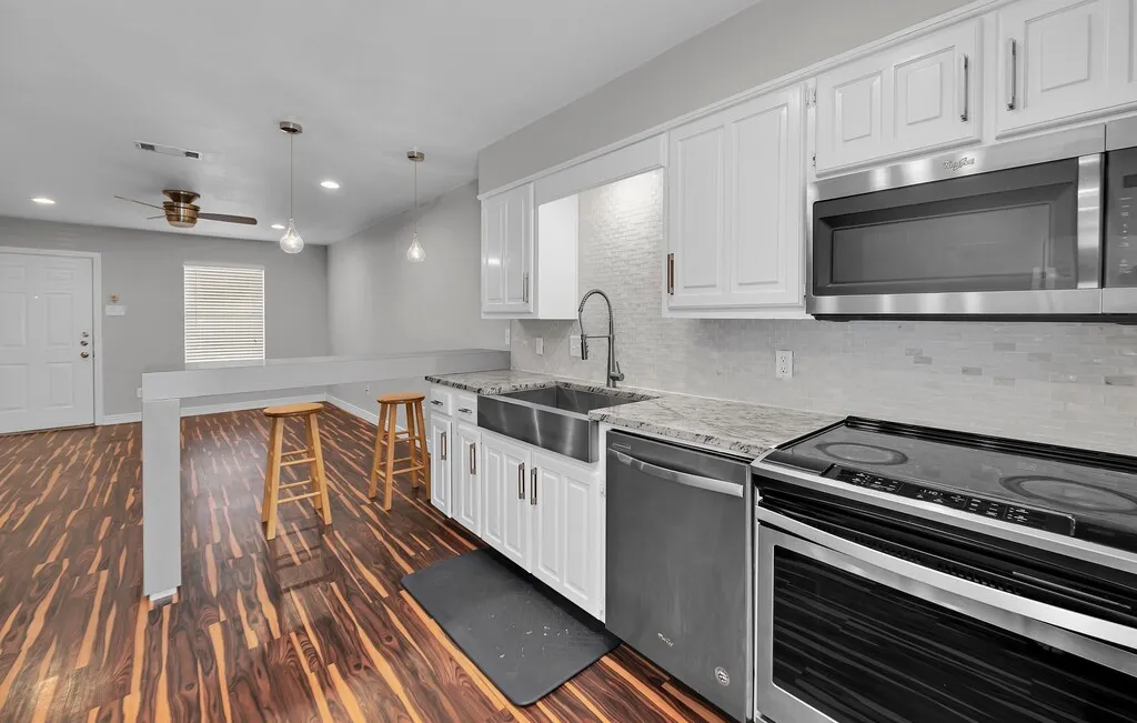 Kitchen featuring white shaker cabinetry, stainless steel appliances, a farmhouse sink, and light-colored countertops