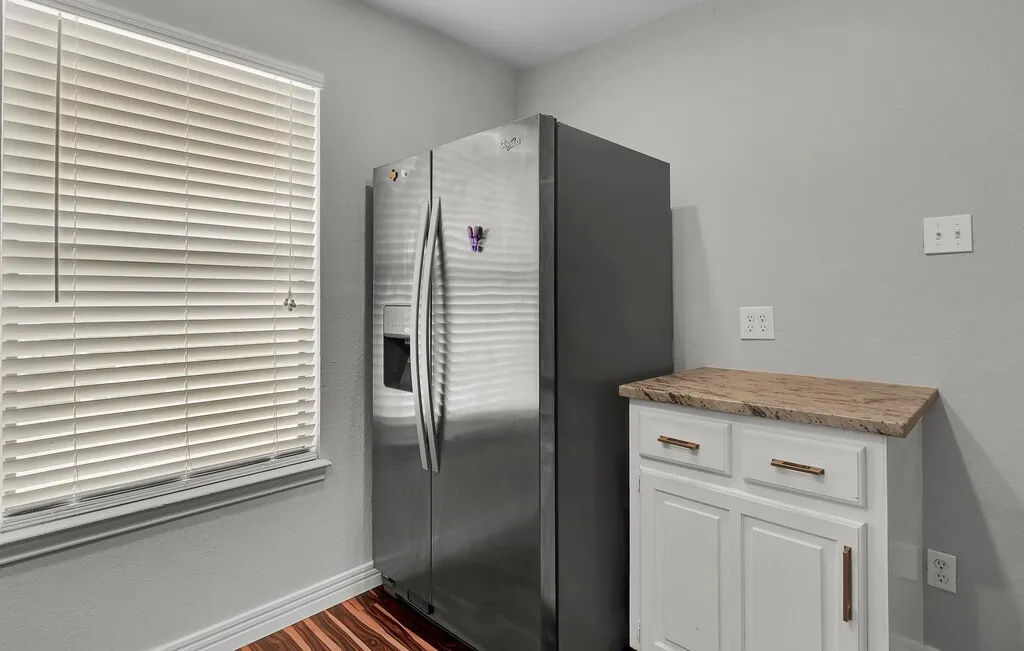 Stainless steel side-by-side refrigerator, white cabinetry with bronze hardware, and wood-finish flooring