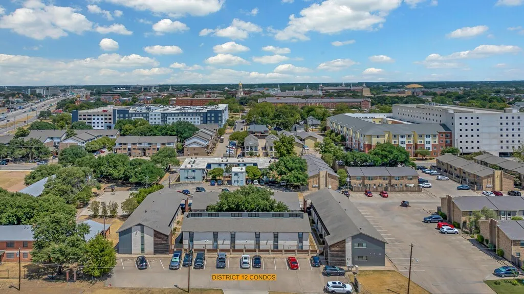 Aerial depiction of District 12 Condos, featuring multiple buildings with gabled roofs, paved parking areas, and mature trees throughout the property