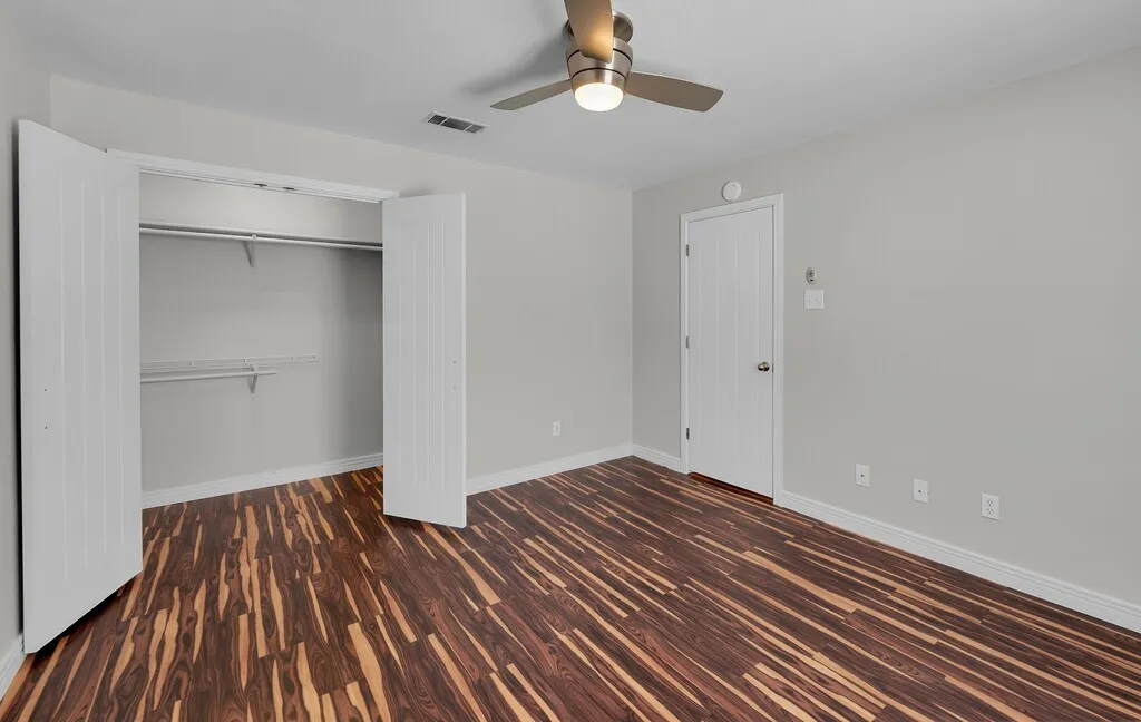 Wood-finish flooring with a horizontal pattern, light gray walls, and a ceiling fan with integrated lighting