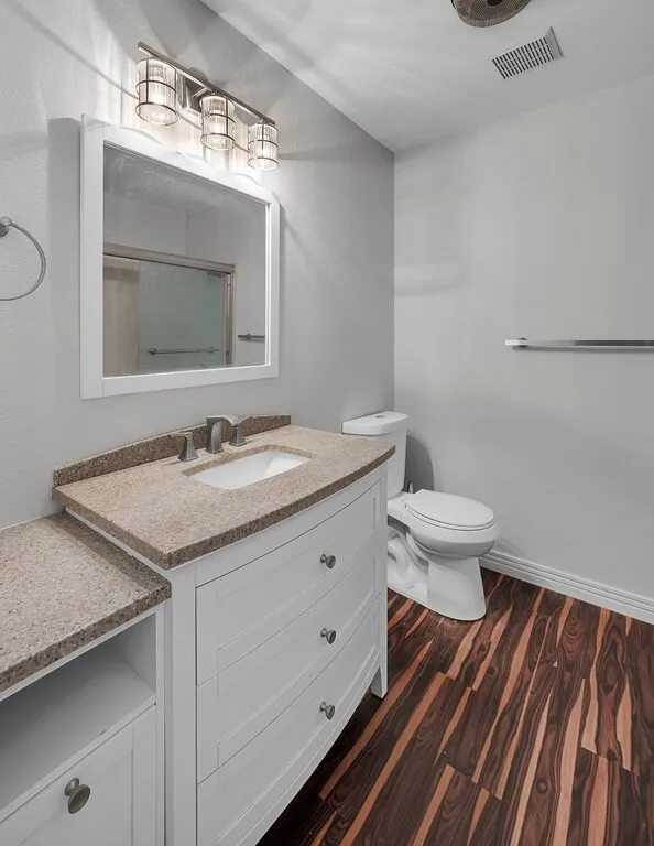 Bathroom featuring a white vanity with an integrated sink, stone-finish countertop, and wood-finish flooring