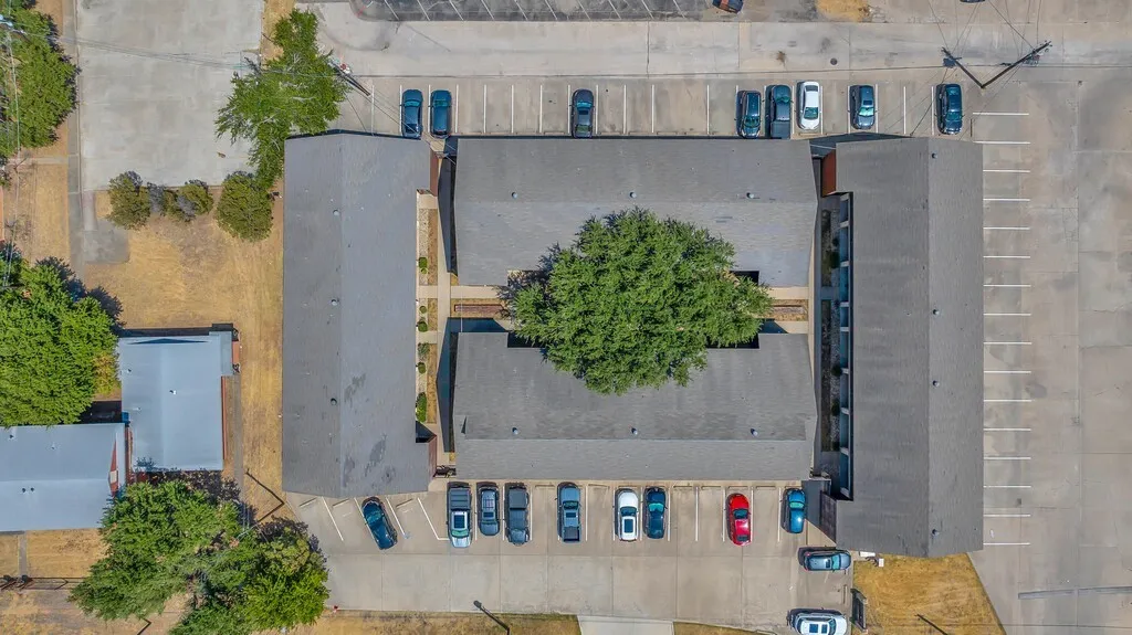 Multiple buildings featuring sloped roofs, a central courtyard with mature trees, and paved parking areas