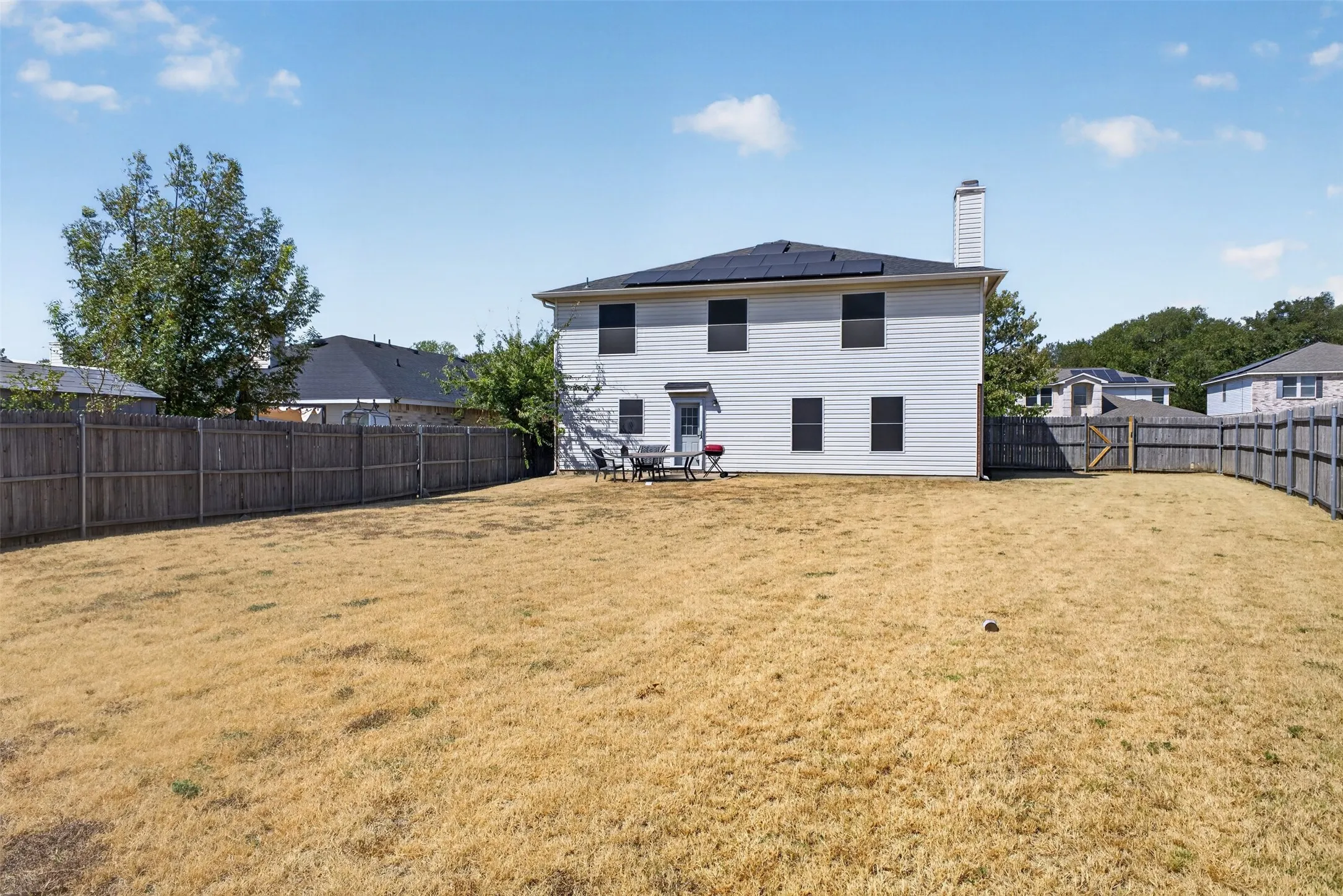 Expansive backyard with wood fencing and a two-story home featuring solar panels and a rear entry door