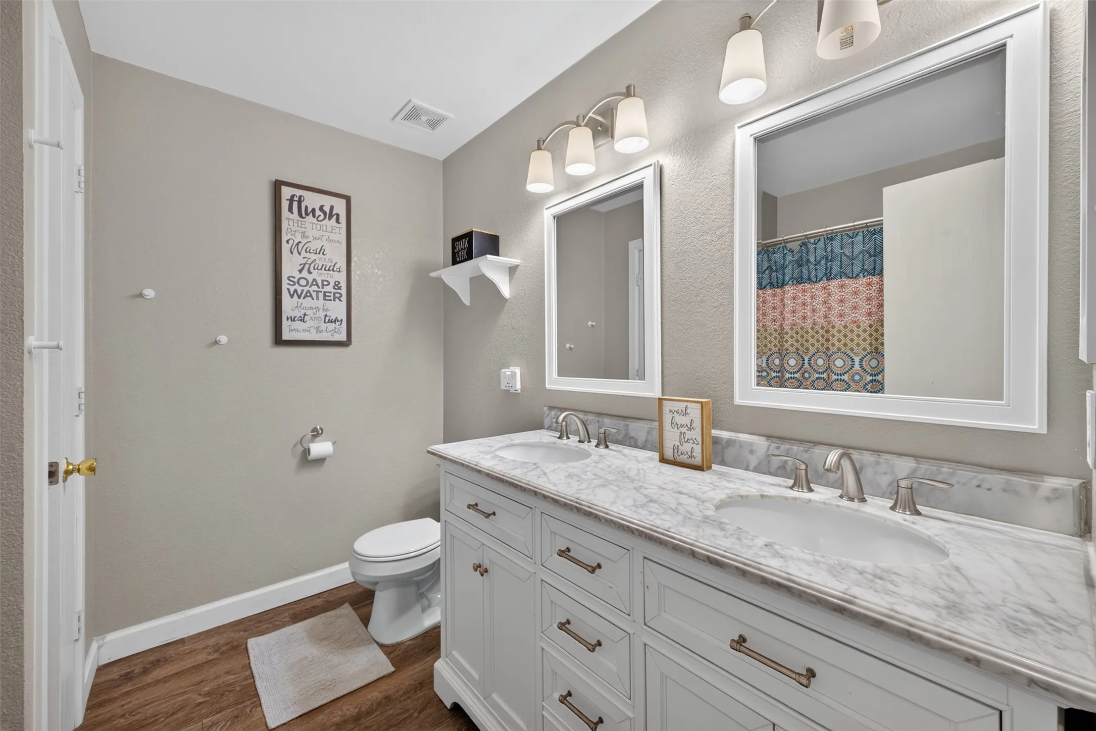 Dual vanity with marble-finish countertop, wood-finish flooring, white cabinetry, and brushed nickel hardware