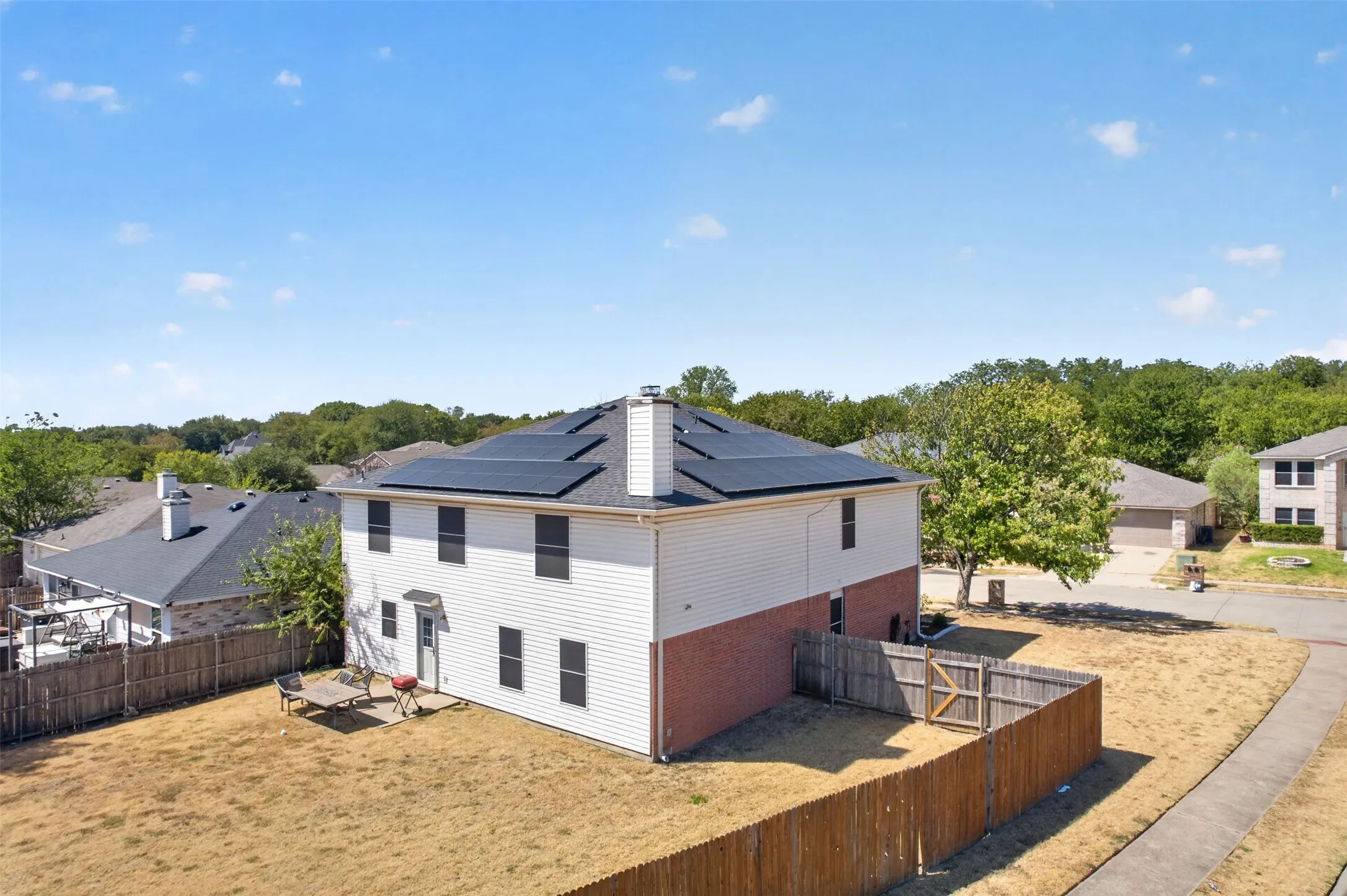 Two-story exterior with brick and siding facade, private backyard, fenced perimeter, and solar panel installation
