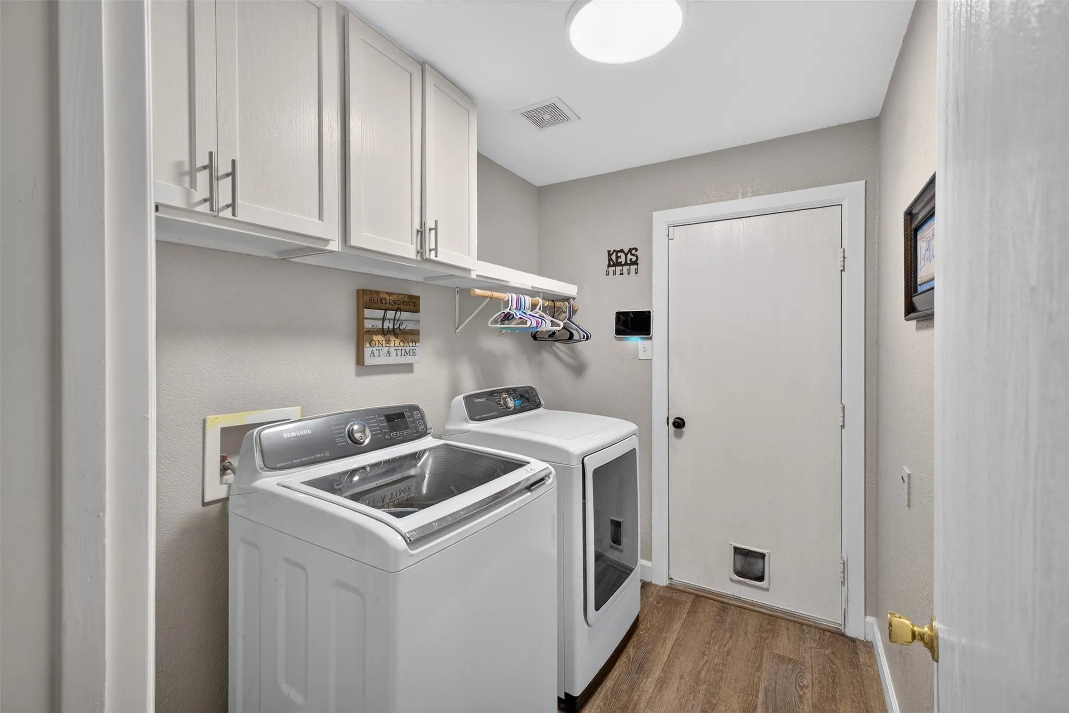 Laundry area featuring wood-finish flooring, overhead cabinetry, and a ceiling-mounted light fixture
