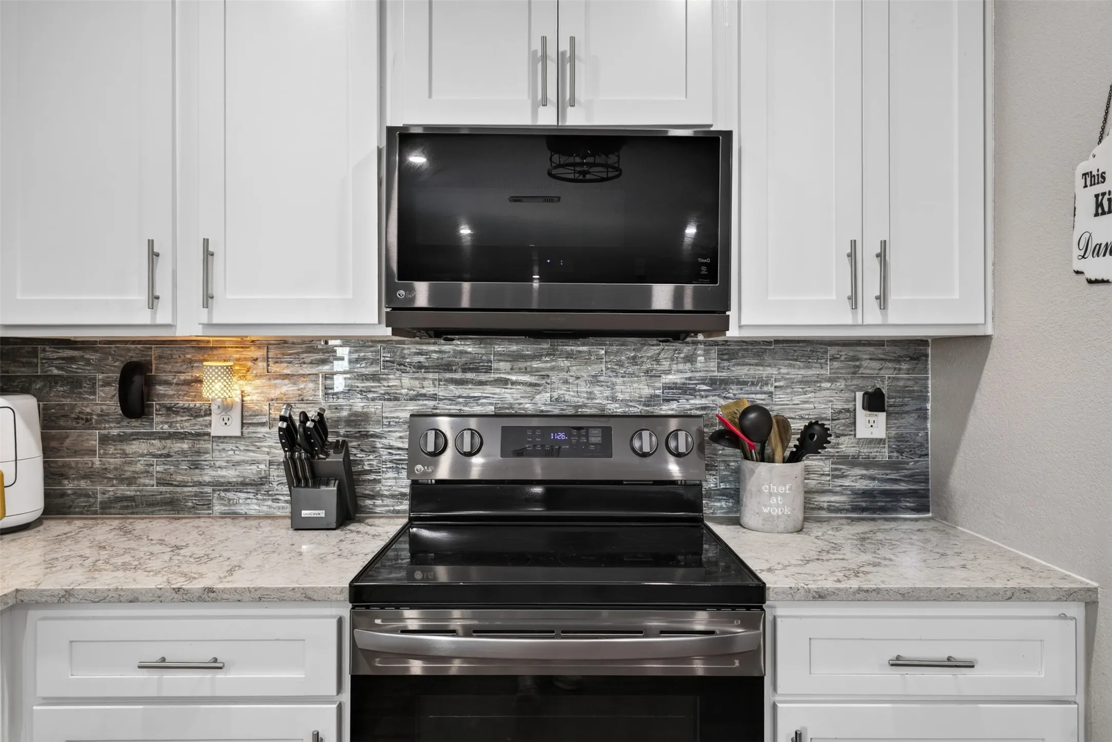 White shaker-style cabinetry, stainless steel appliances, a textured tile backsplash, and light-toned countertops