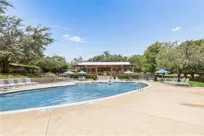 Resort-style swimming pool with a large surrounding deck, surrounded by mature trees, with a covered outdoor lounge area