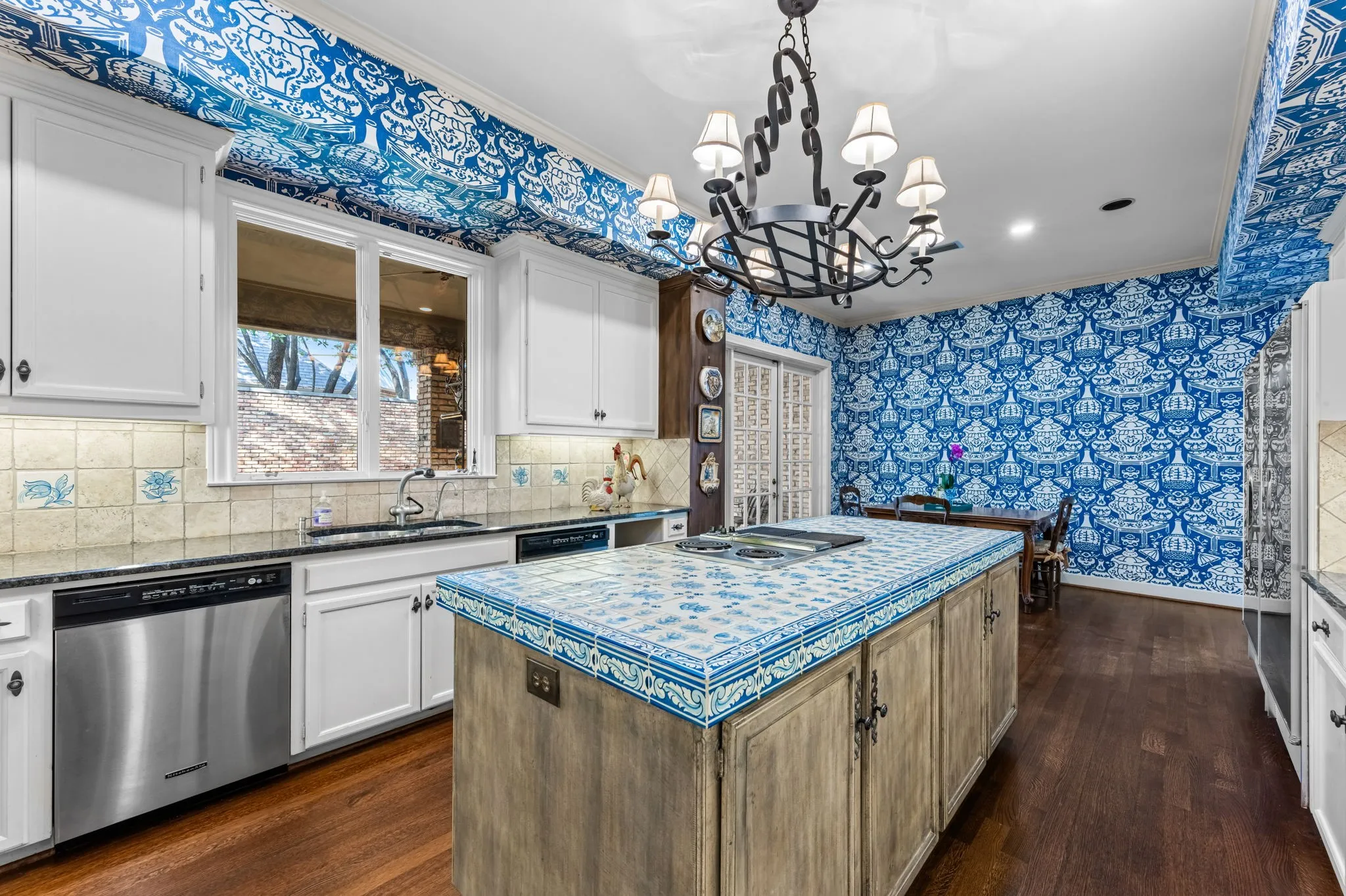 Wood-finish flooring, white cabinetry, blue tiled island, stainless steel appliances, and a wrought iron chandelier