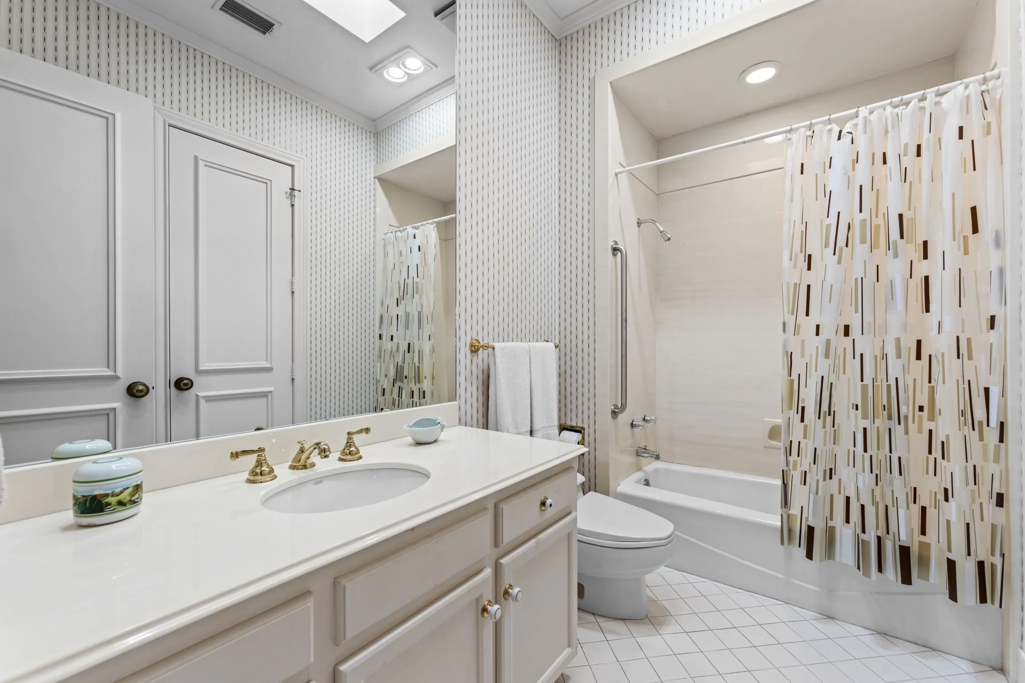 White vanity with an integrated sink, polished brass faucet, and white tiled flooring