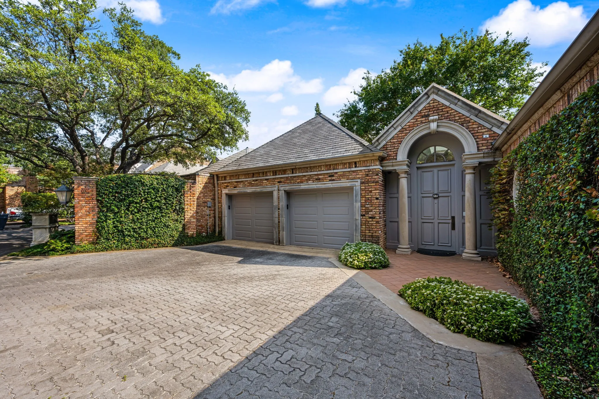 Brick facade with stone accents, arched entry with double doors, two-car garage, and mature landscaping