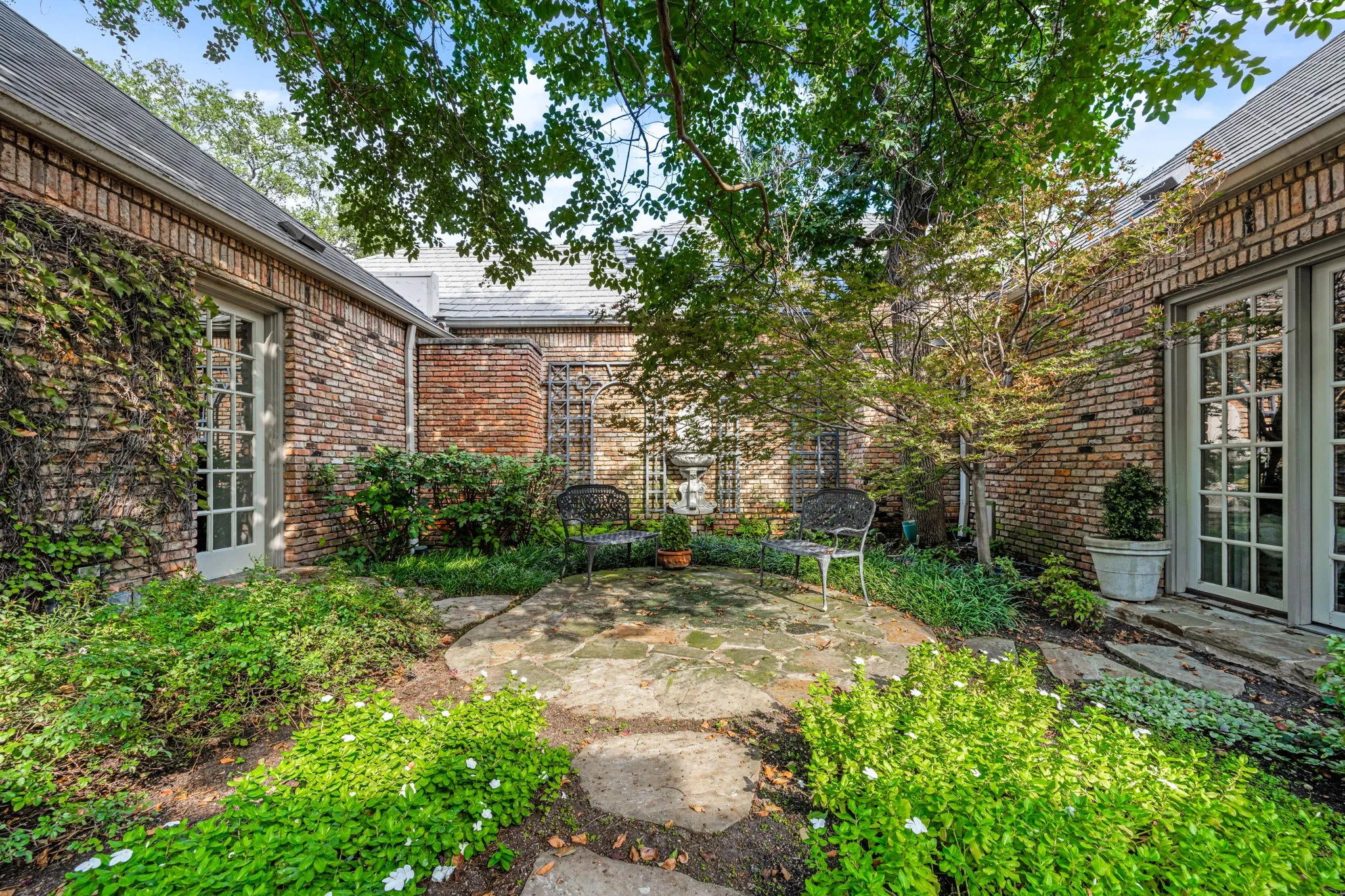 Private courtyard featuring a stone patio, mature trees, and garden beds