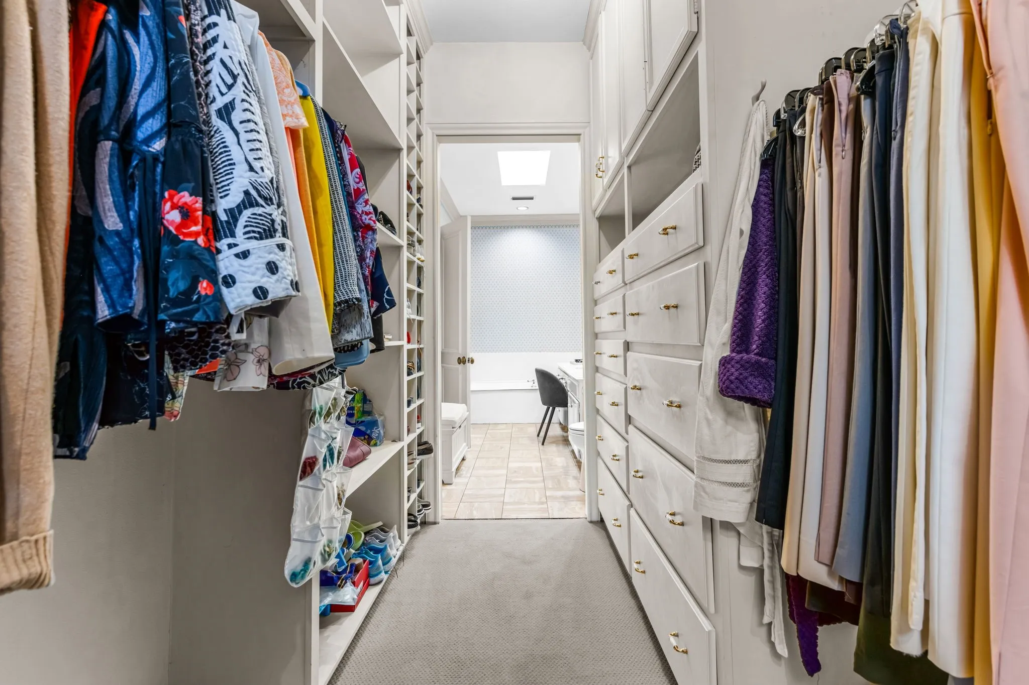Custom built-in cabinetry, integrated shelving, hanging storage, white wood-finish drawers with gold-tone hardware, and carpet flooring