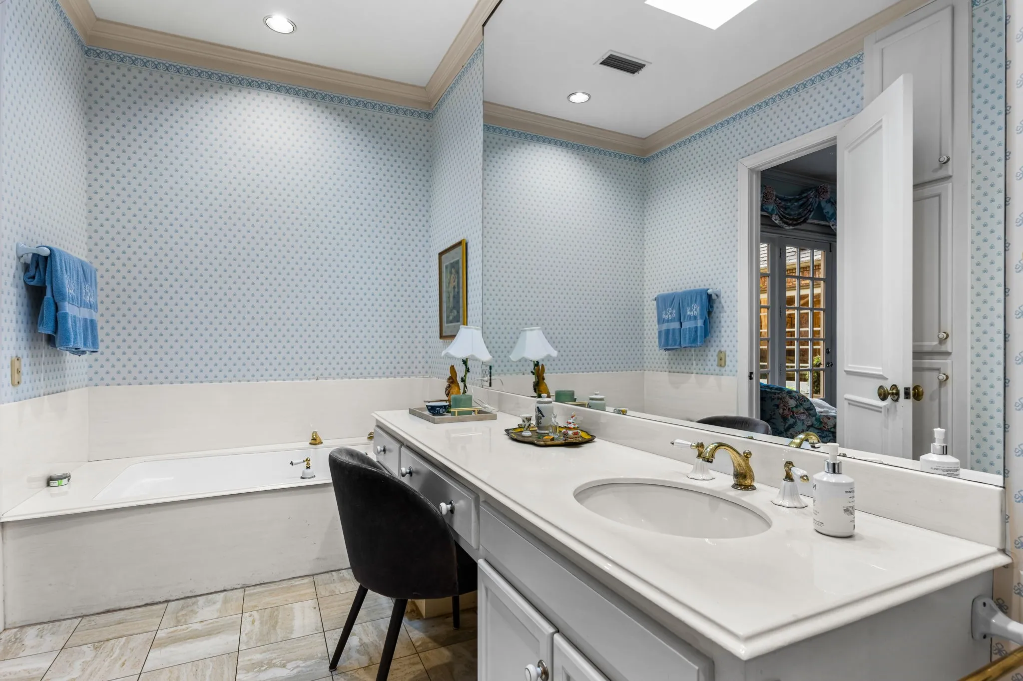 Built-in bathtub, extensive vanity with integrated sink, polished brass-finish faucet, overhead recessed lighting, and wall-mounted storage cabinetry