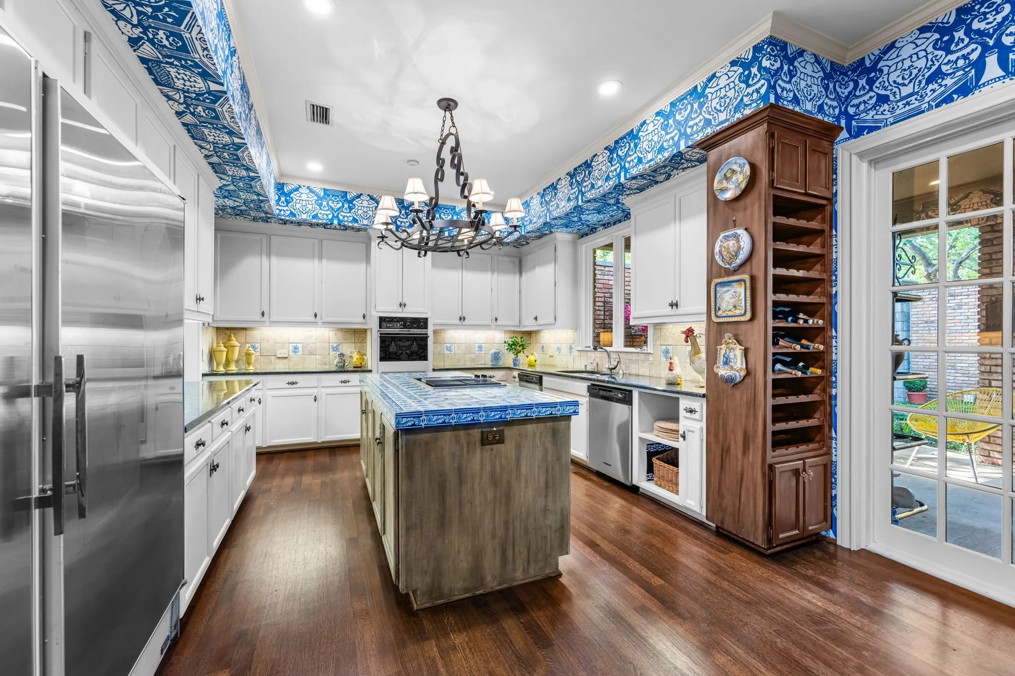 Kitchen featuring hardwood flooring, white cabinetry, stainless steel appliances, a tiled island with seating, and a built-in wine rack