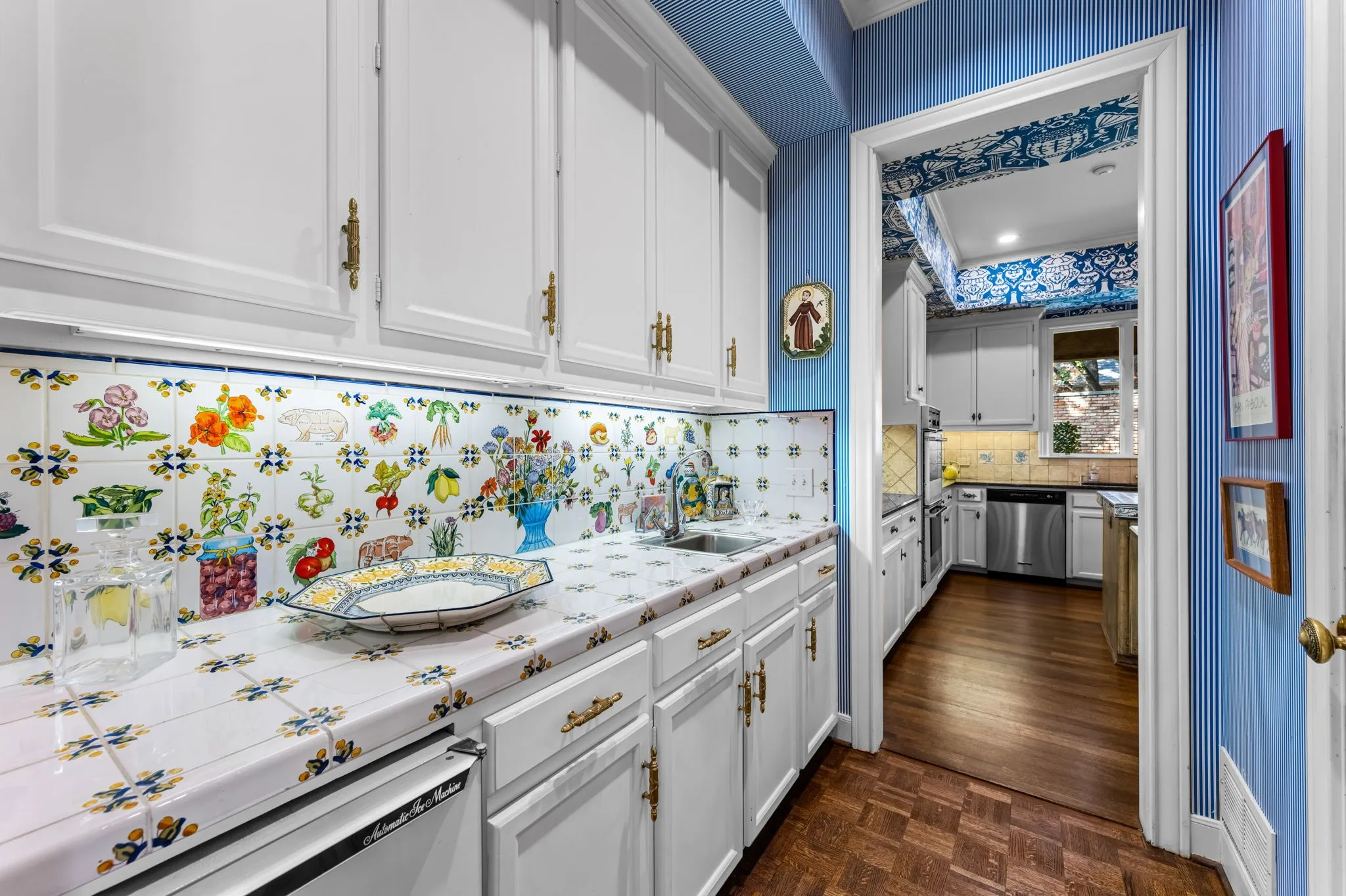 Butlers Pantry white cabinetry with brass-toned hardware, ceramic tile countertops, patterned tile backsplash, and a built-in dishwasher