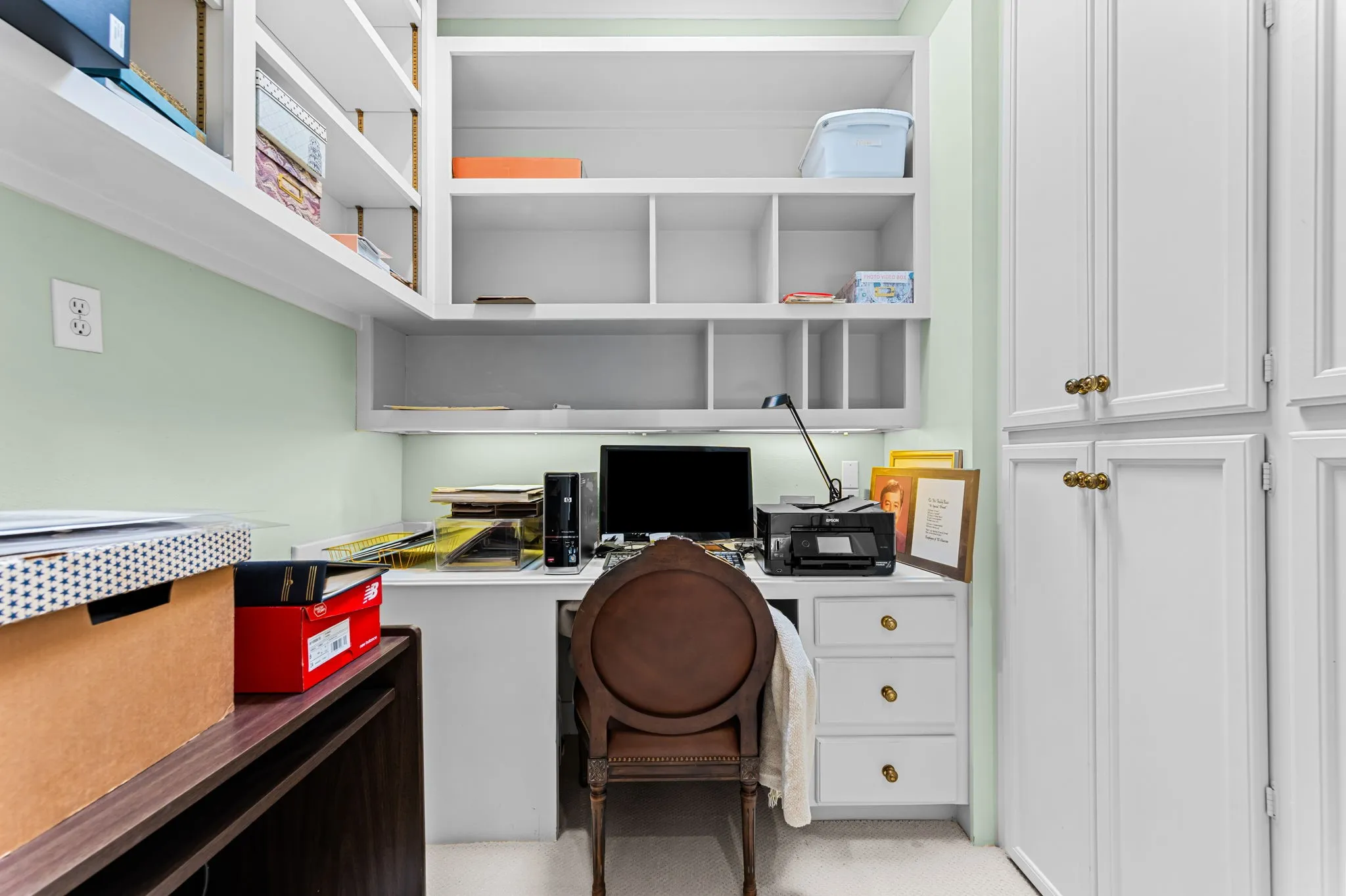 Built-in desk with task lighting, integrated shelving, and white cabinetry featuring brass-finish hardware