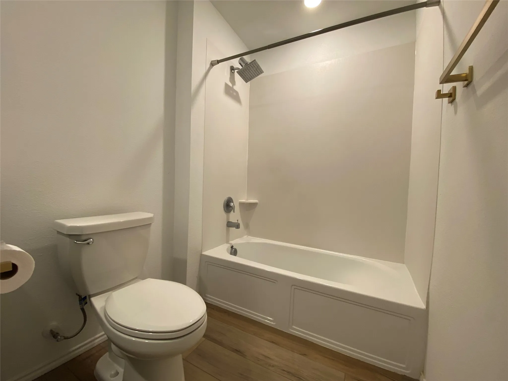 Bathroom with shower / tub combination, wood finished floors, and toilet