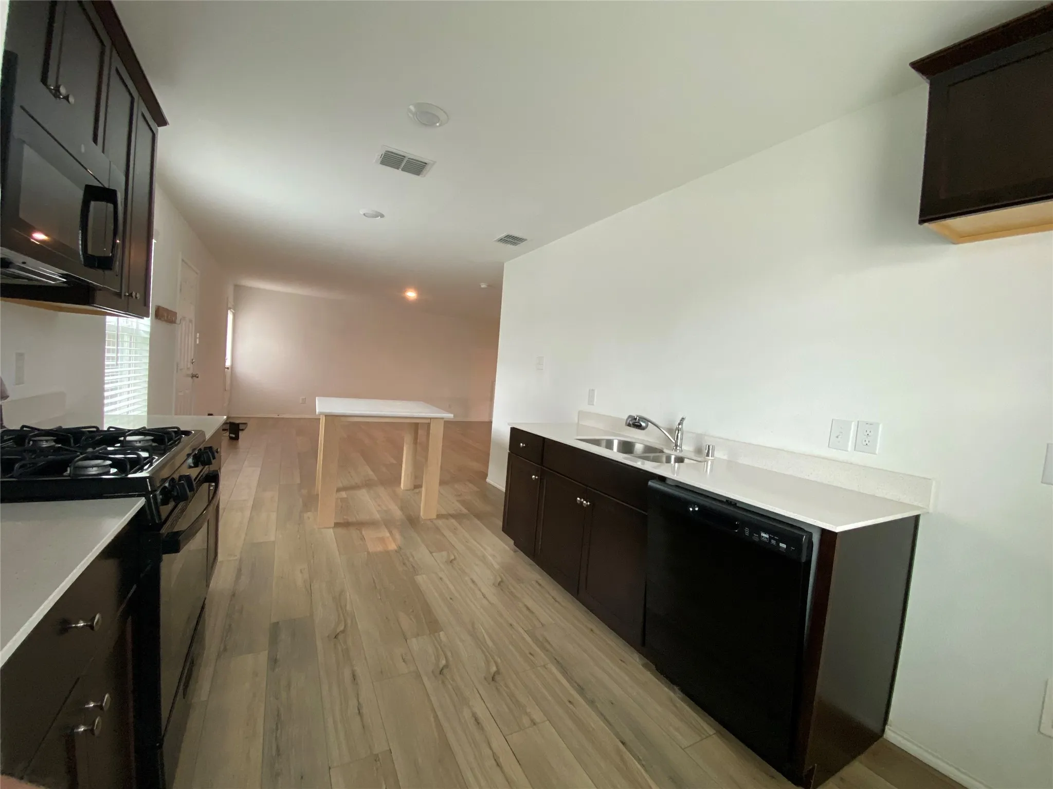Kitchen featuring light countertops, visible vents, light wood finished floors, a sink, and black appliances