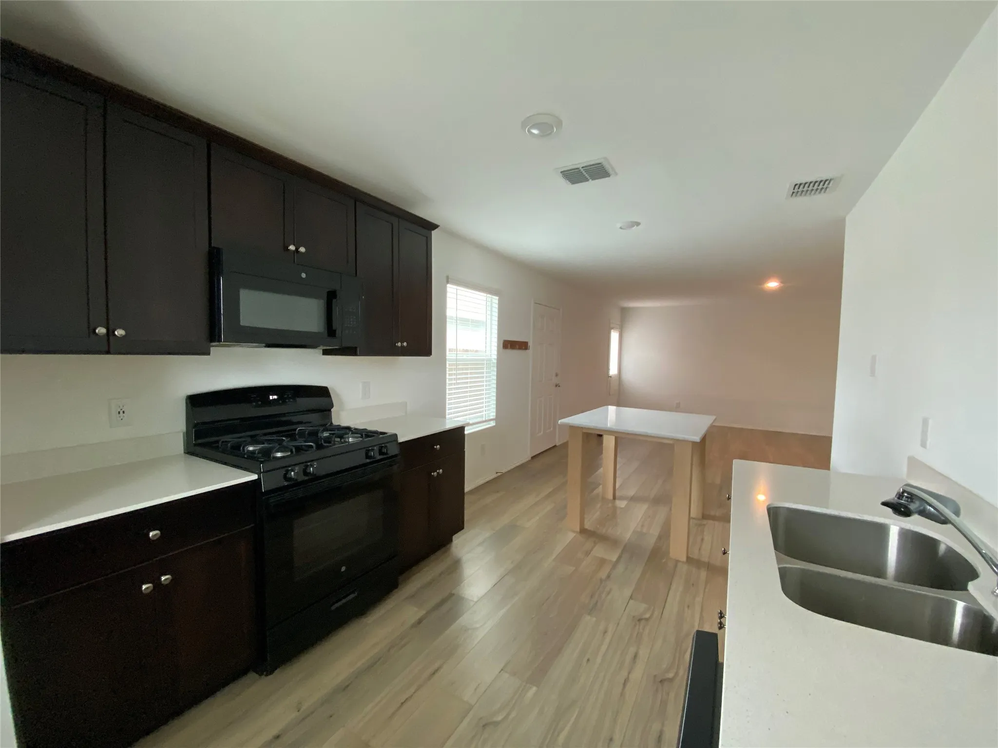 Kitchen featuring dark cabinetry, a sink, light wood-style floors, visible vents, and black appliances