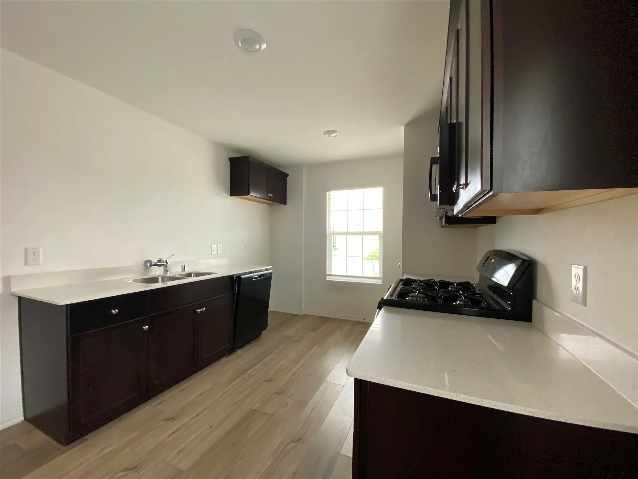 Kitchen featuring black appliances, light wood-style flooring, a sink, and light stone counters