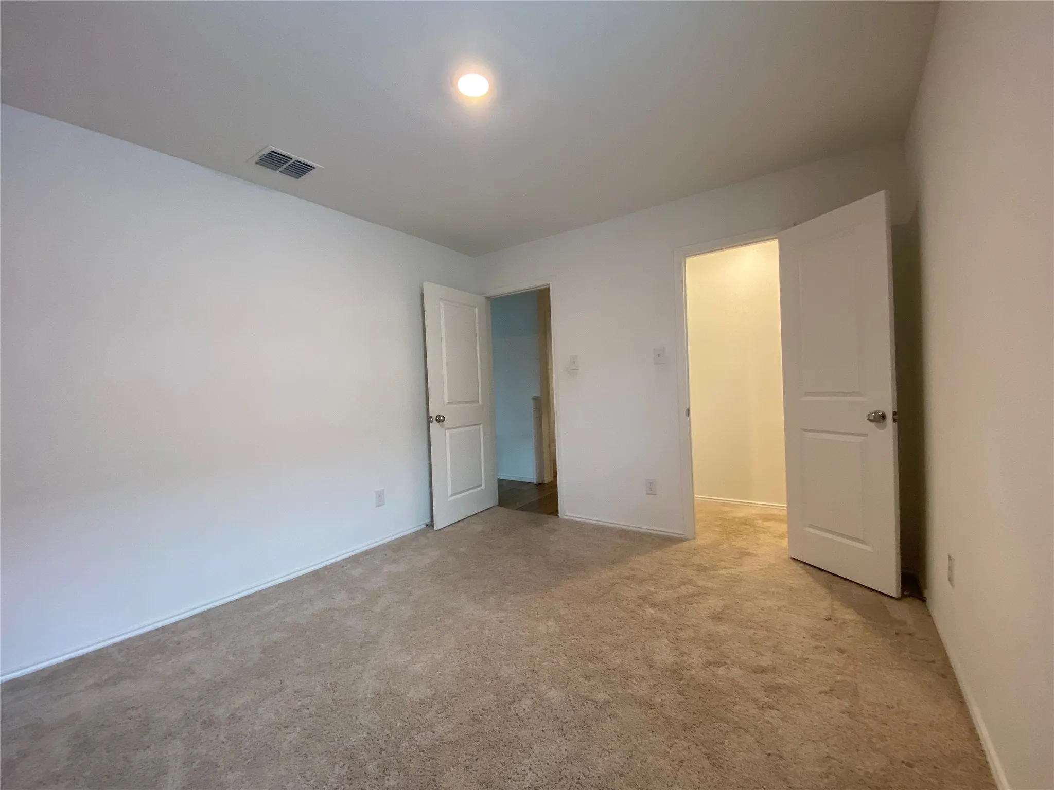Unfurnished bedroom with light colored carpet, visible vents, and baseboards