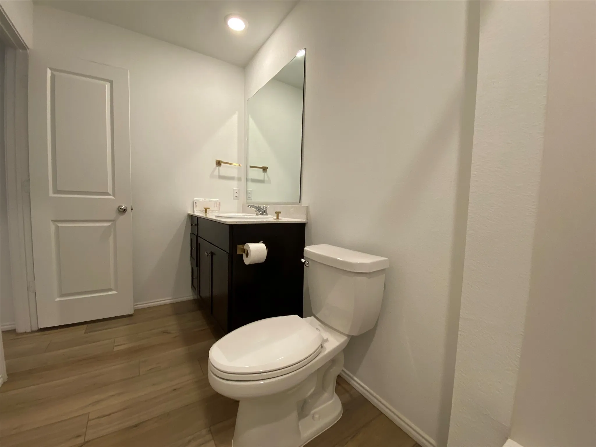Half bath with toilet, wood finished floors, baseboards, and vanity