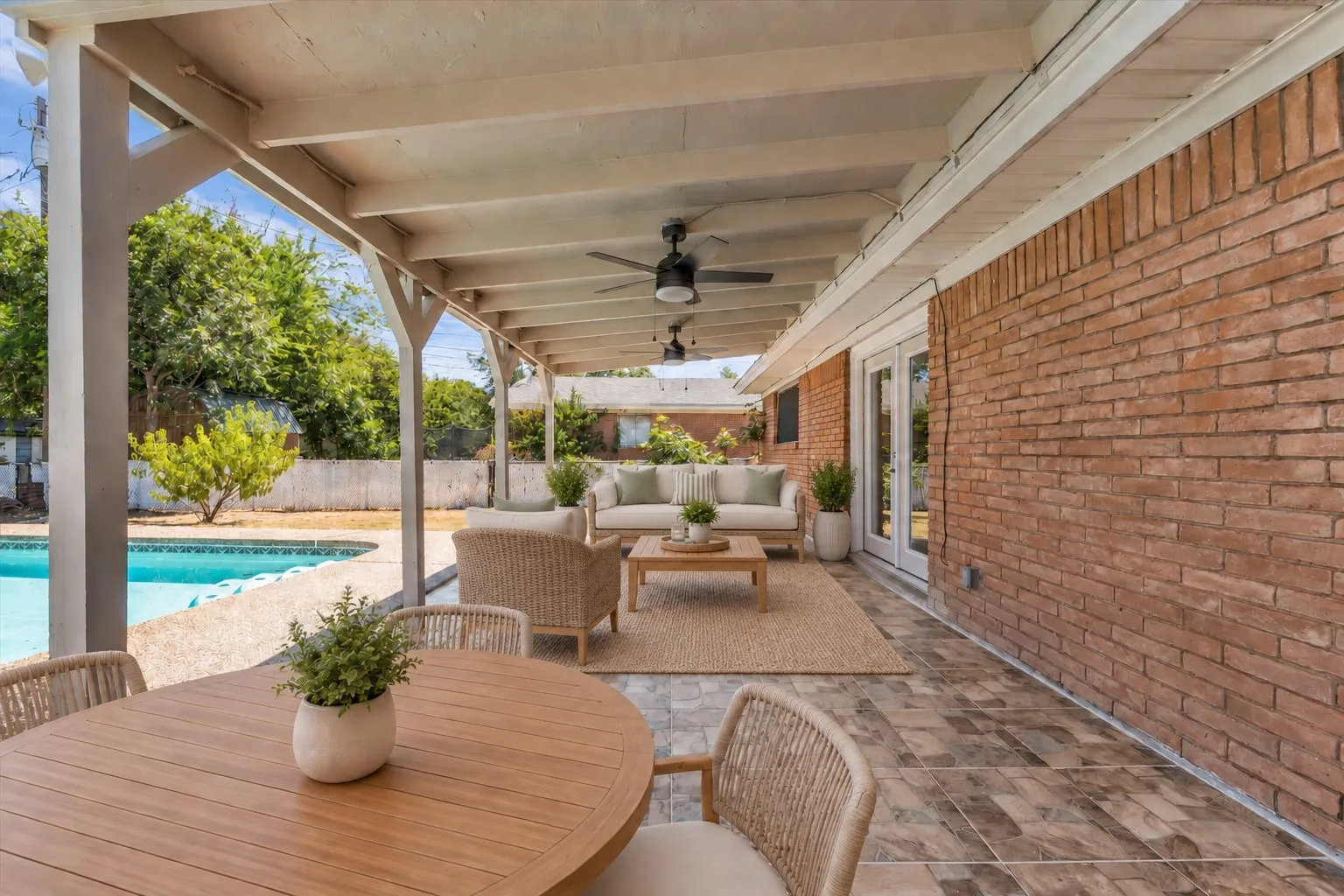 Expansive covered patio with exposed beam ceiling, ceiling fans, brick exterior, and direct access to a swimming pool , Virtually Staged