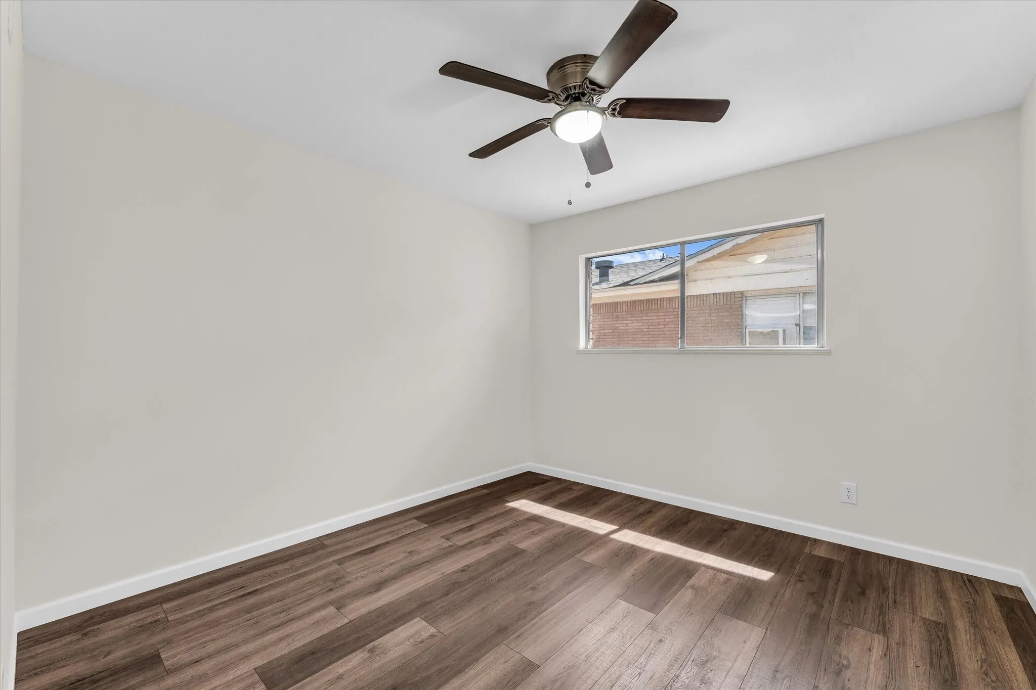 Wood-finish flooring with white trim, a ceiling fan with integrated lighting, and a window providing natural light