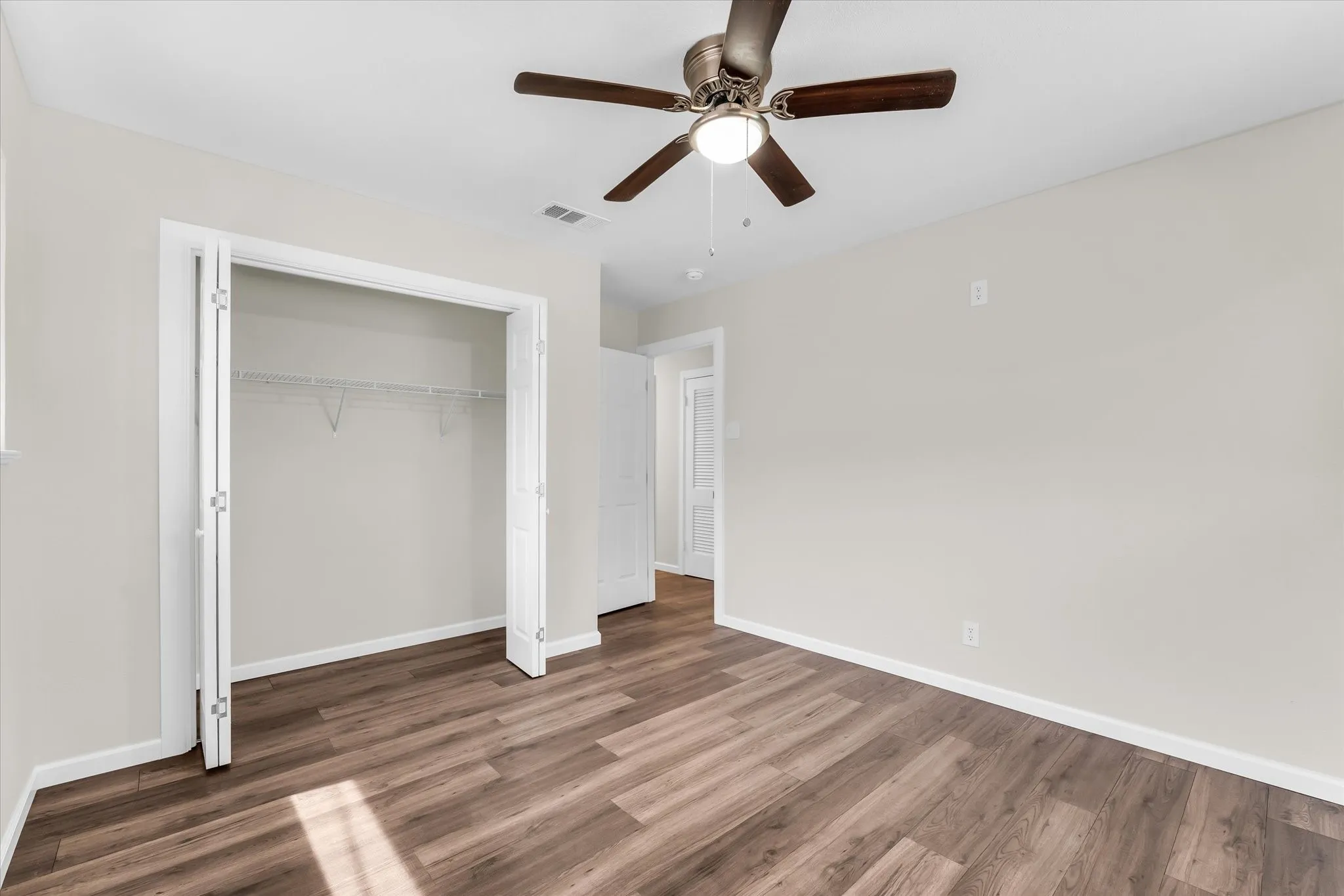 Wood-finish flooring, ceiling fan with integrated lighting, bi-fold closet doors, and light neutral wall tones