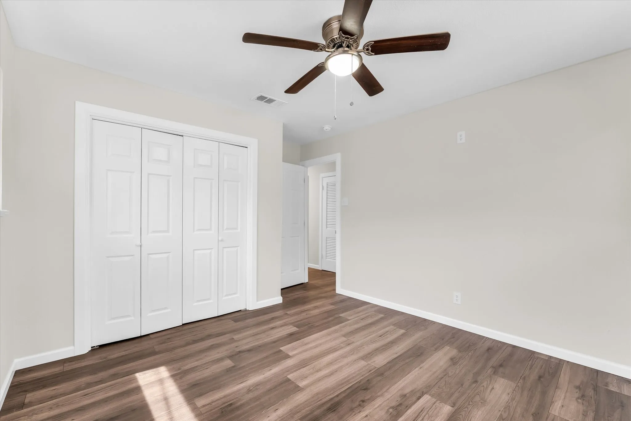 Wood-finish flooring, white bi-fold closet doors, ceiling fan with integrated lighting, and neutral wall paint