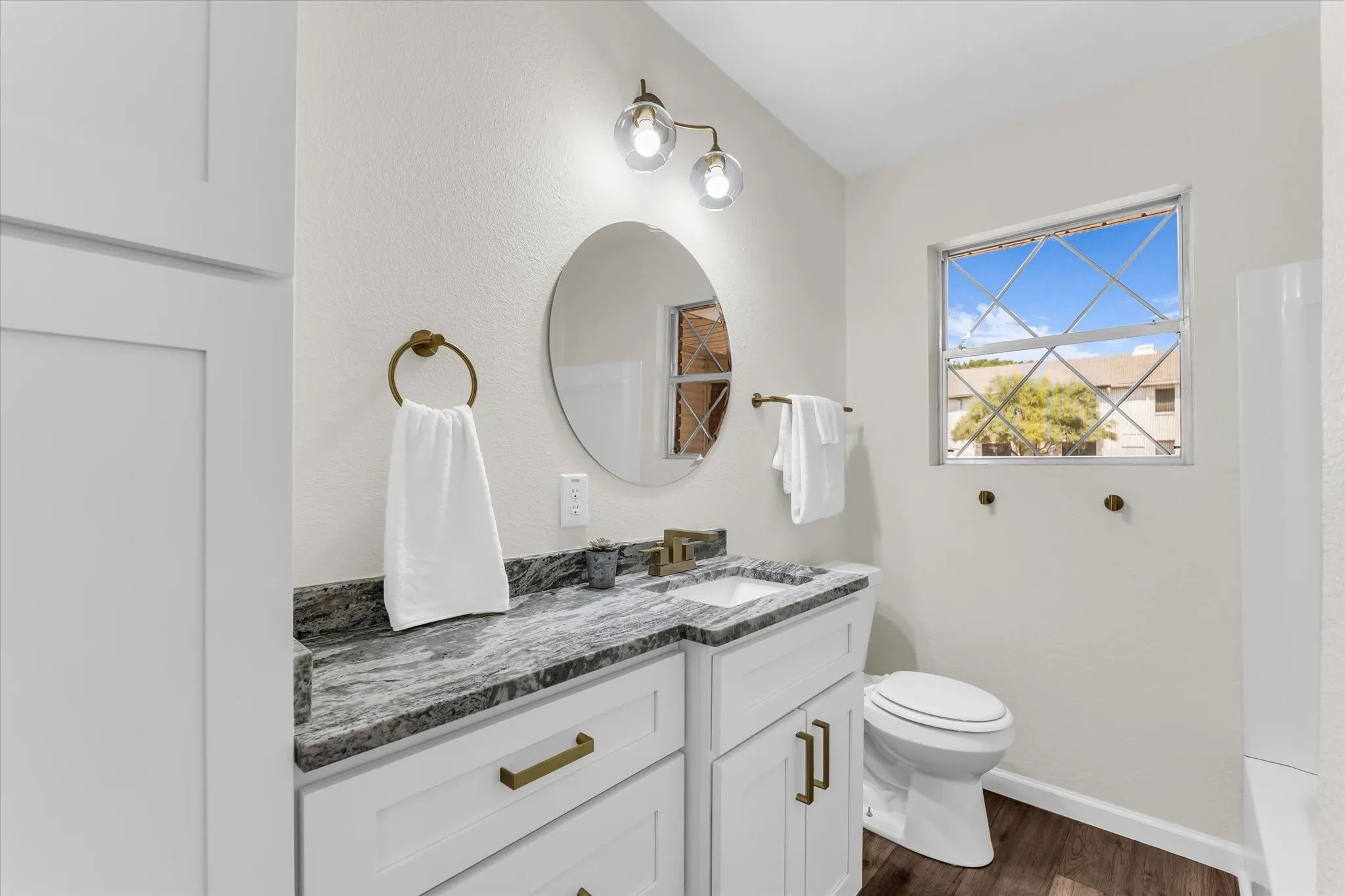 White vanity with brass hardware, undermount sink, and a dark stone countertop