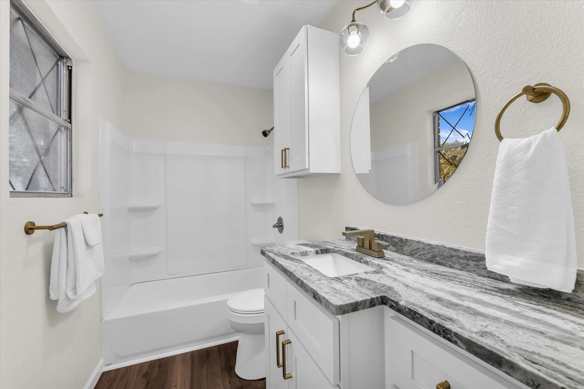 White vanity with a rectangular undermount sink, a gray patterned countertop, and brass-finish hardware
