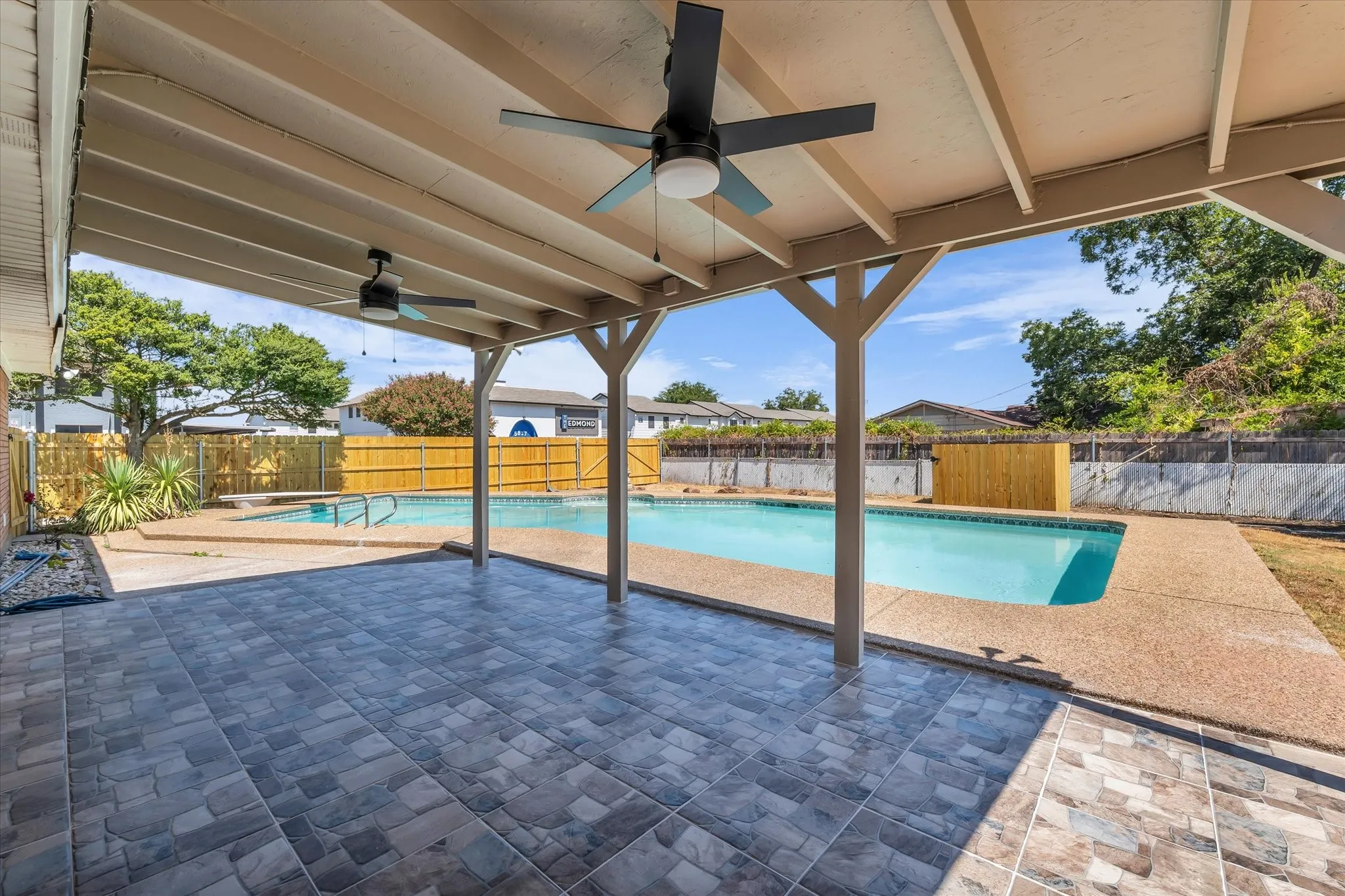 Covered patio with large format tile flooring, supported by wood posts, featuring ceiling fans and an in-ground swimming pool
