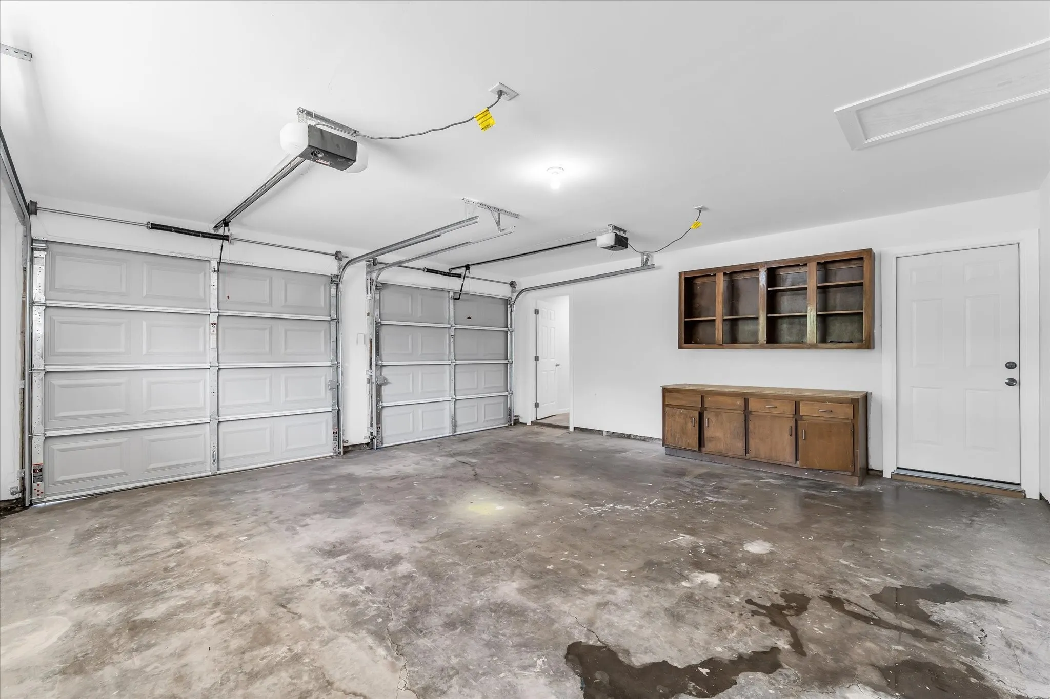 Two vehicle access doors with automatic openers, concrete flooring, built-in wood cabinetry, and a service door