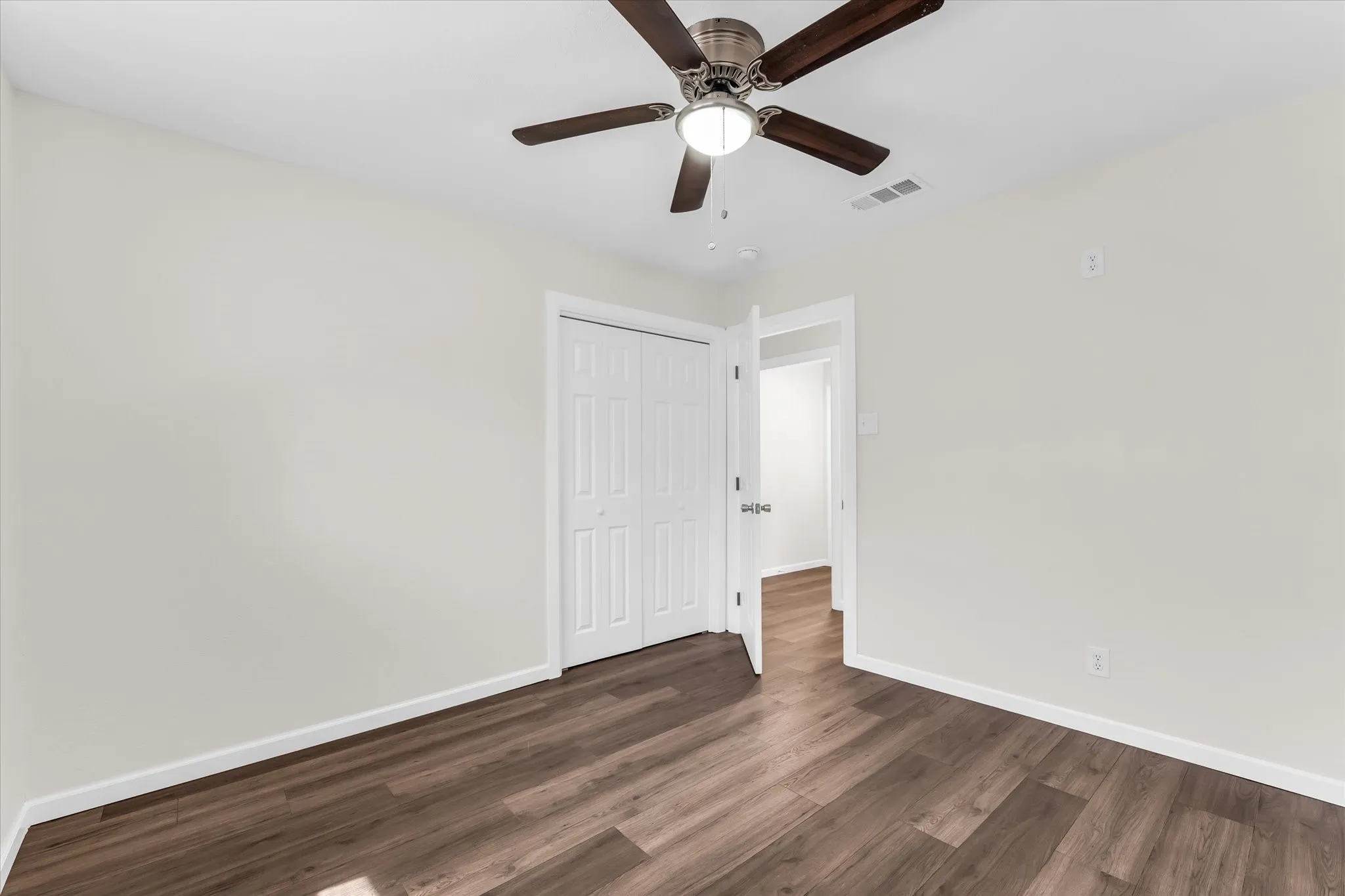 Wood-finish flooring with white trim, a ceiling fan with light fixture, and white bi-fold closet doors