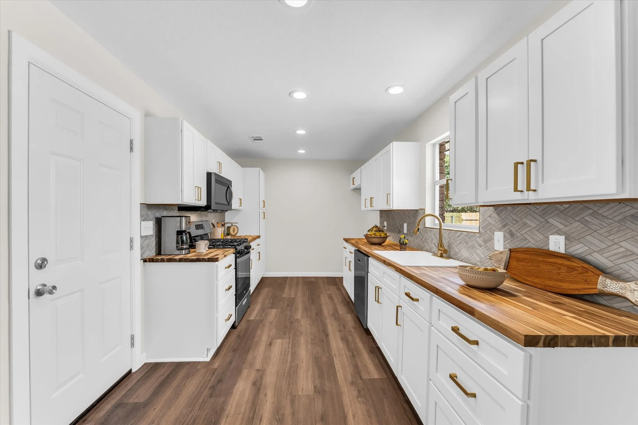 Galley kitchen featuring white cabinetry with gold-tone hardware, wood-finish countertops, black appliances, and recessed lighting