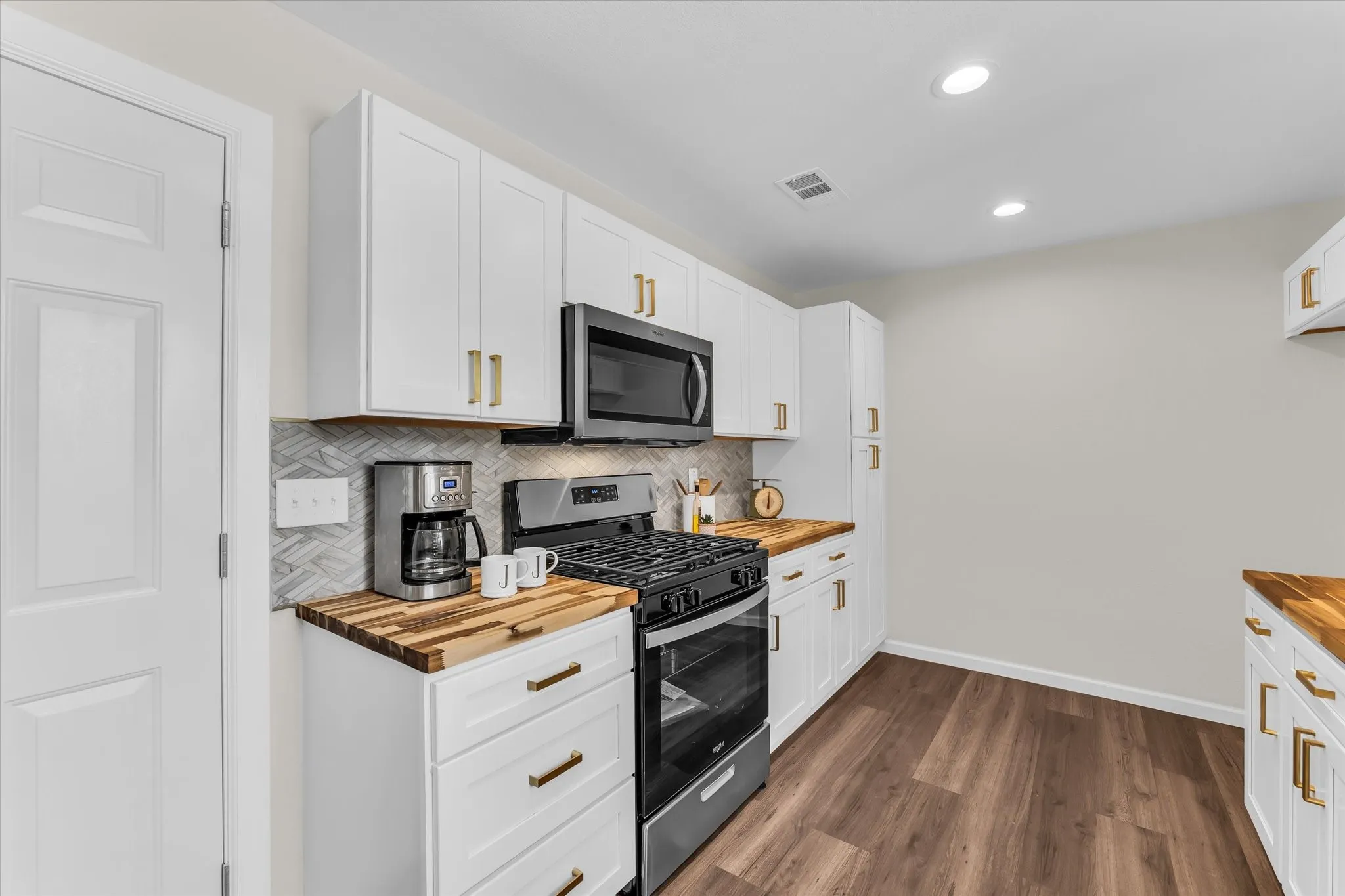 Kitchen featuring white cabinetry, wood-finish countertops, stainless steel appliances, a herringbone tile backsplash, and recessed lighting