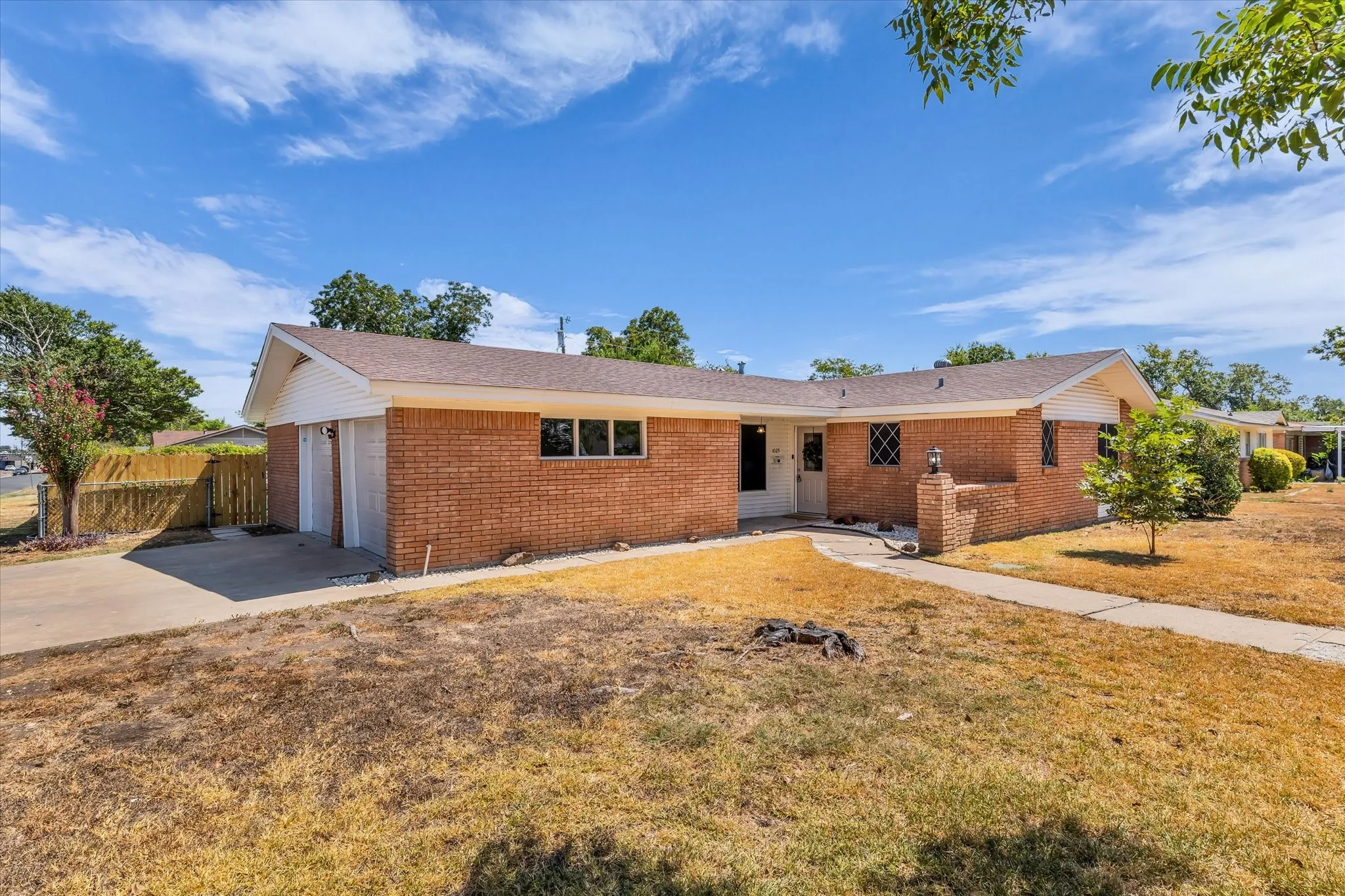 Expansive backyard featuring a swimming pool with integrated steps, a covered patio with a paved surface, and a brick exterior, virtually staged
