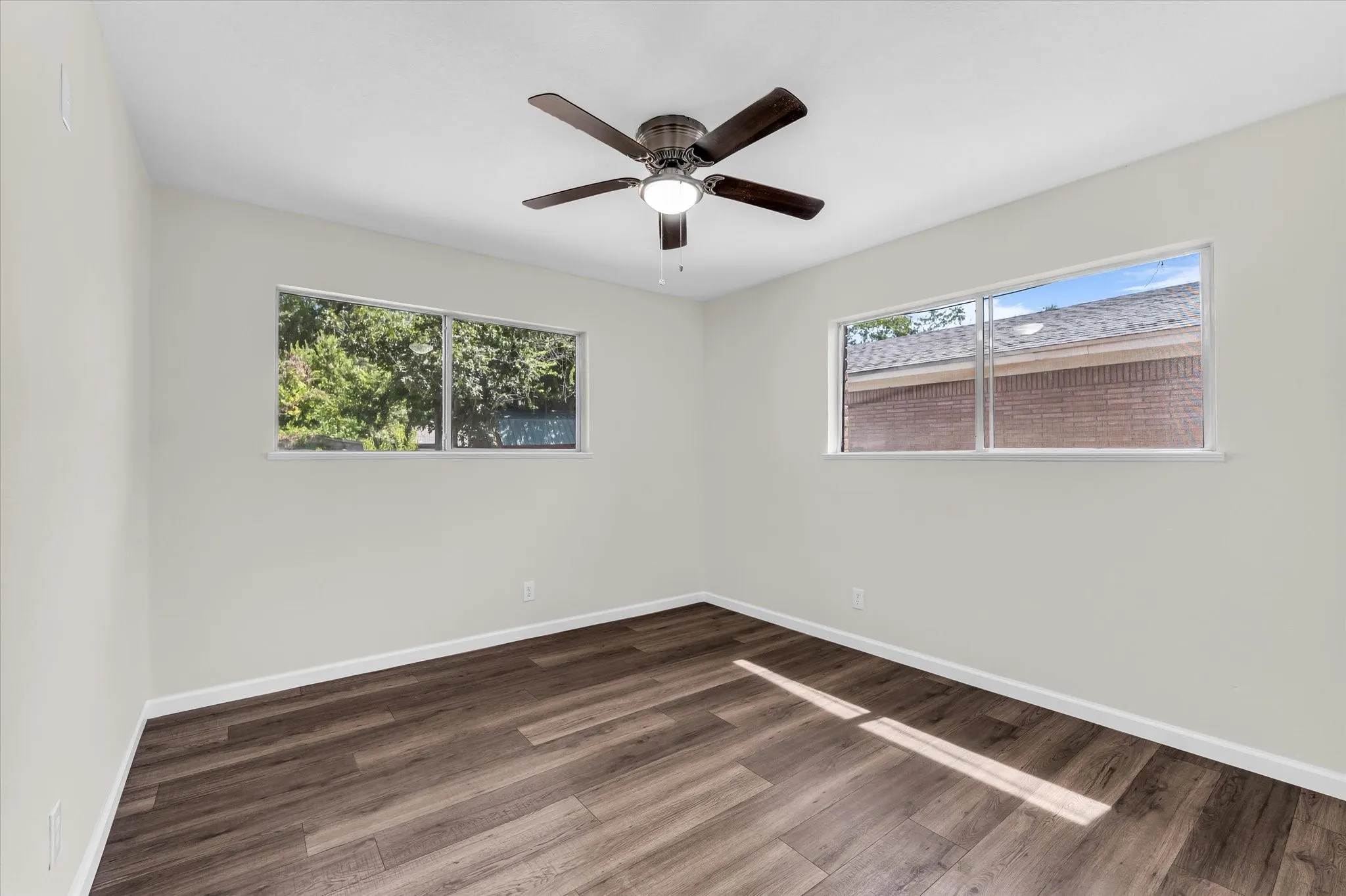 Spacious interior featuring wood-finish flooring, light-toned walls, a ceiling fan with integrated lighting, and two large windows