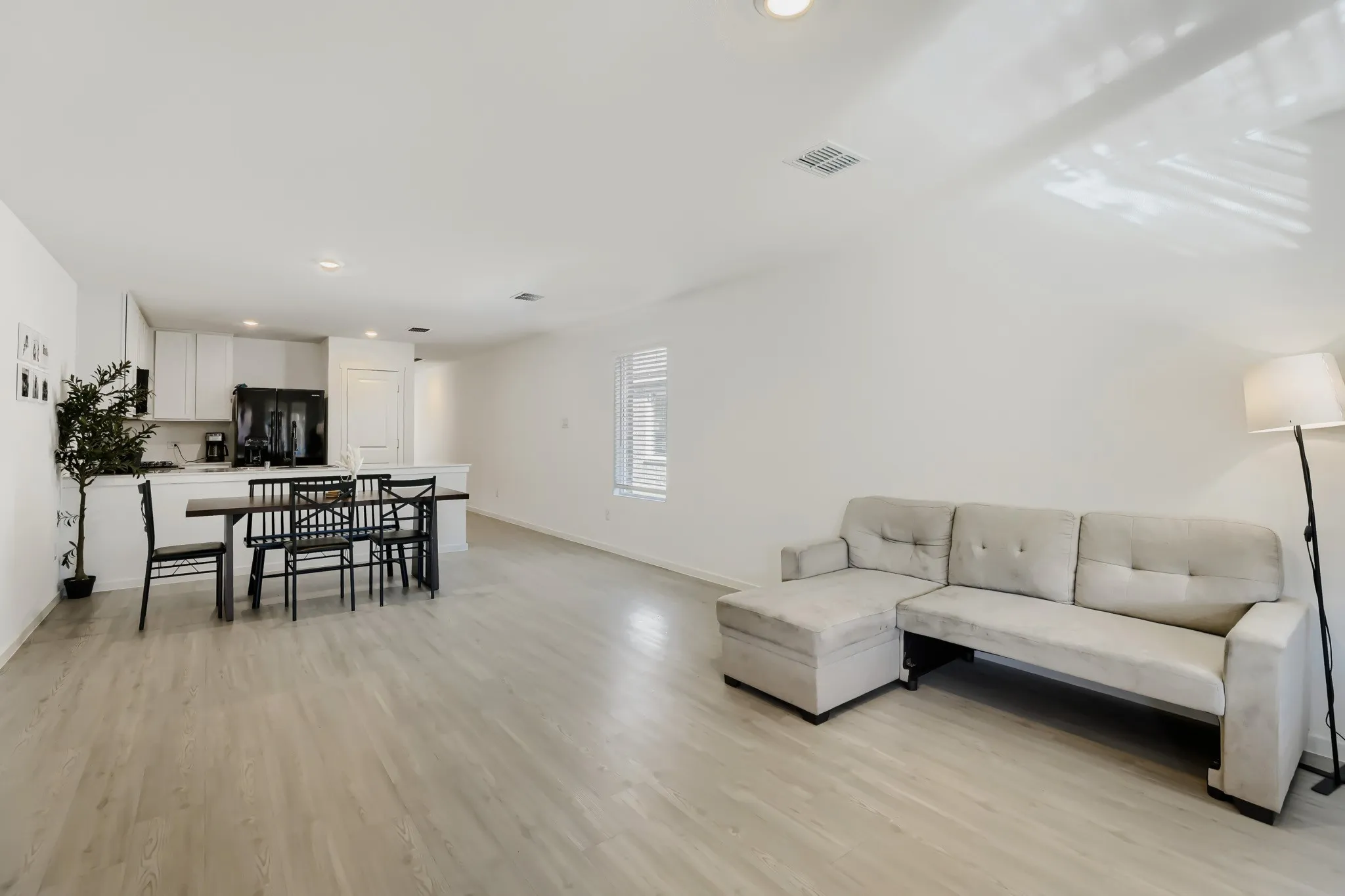 Open-concept living space featuring wood-finish flooring, recessed lighting, and a kitchen with white cabinetry and black appliances