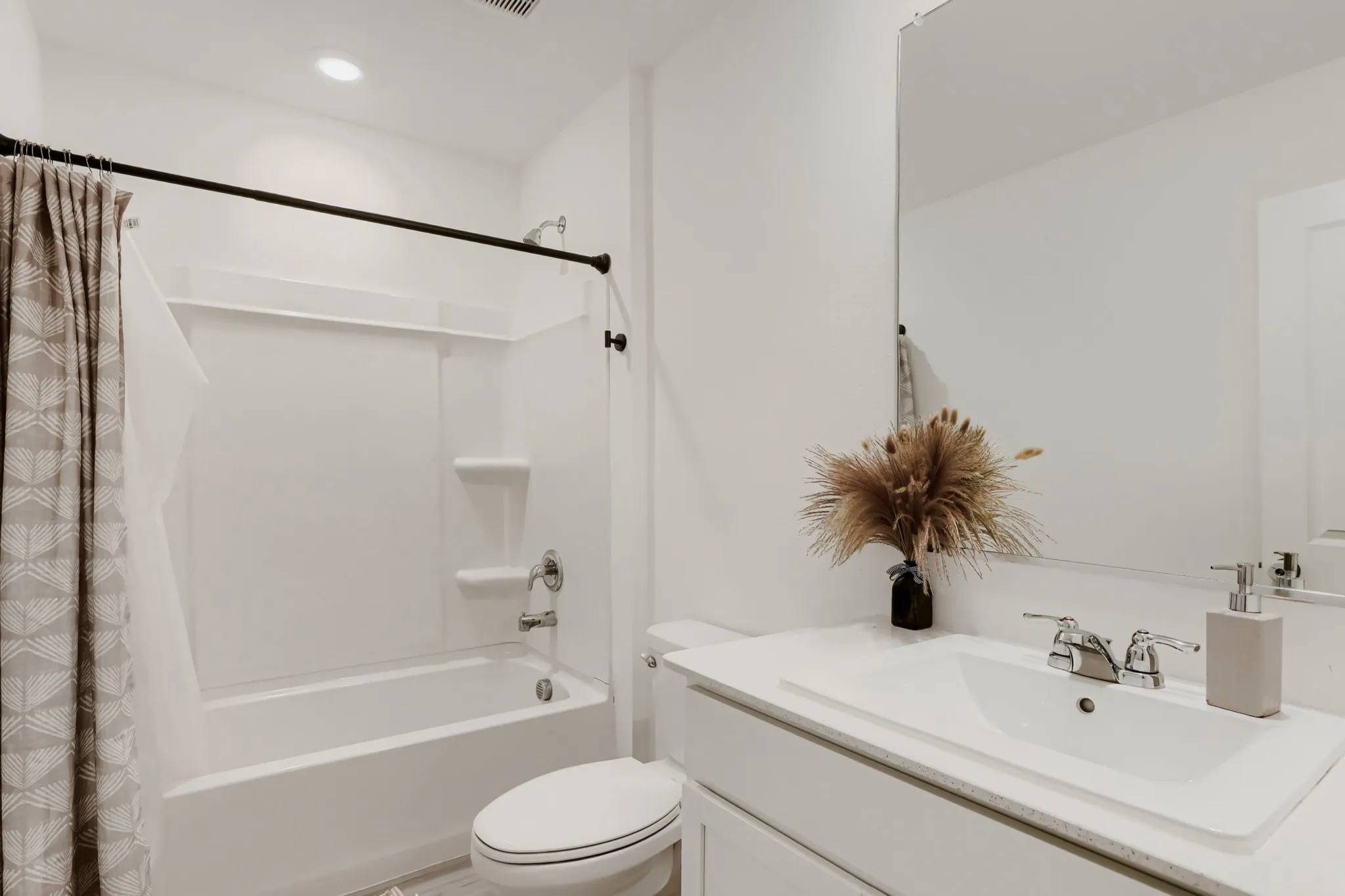 Bathroom featuring a white integrated tub and shower, a single vanity with an integrated sink, a large wall-mounted mirror, and chrome fixtures