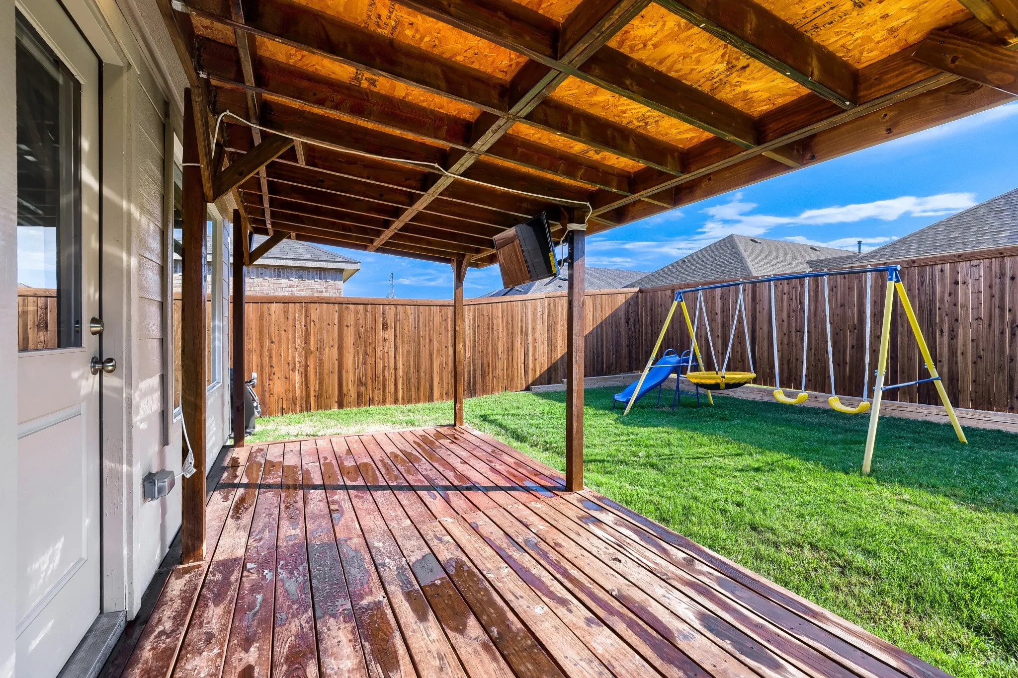 Covered wood deck with exposed wood rafters, overlooking a fenced yard with a manicured lawn