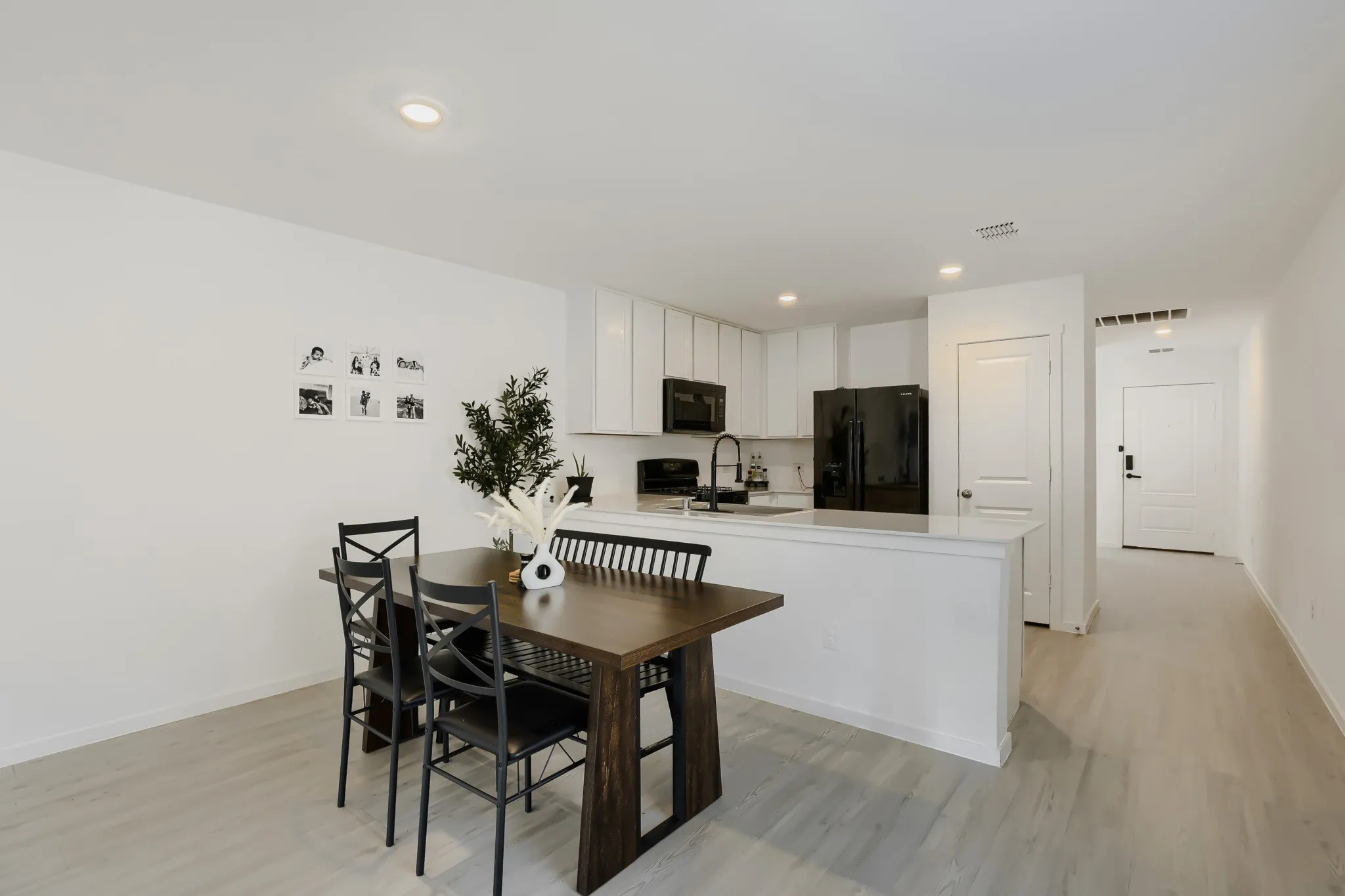 Light wood-finish flooring, white walls, recessed lighting, and a kitchen featuring white cabinetry, a white countertop, and black appliances