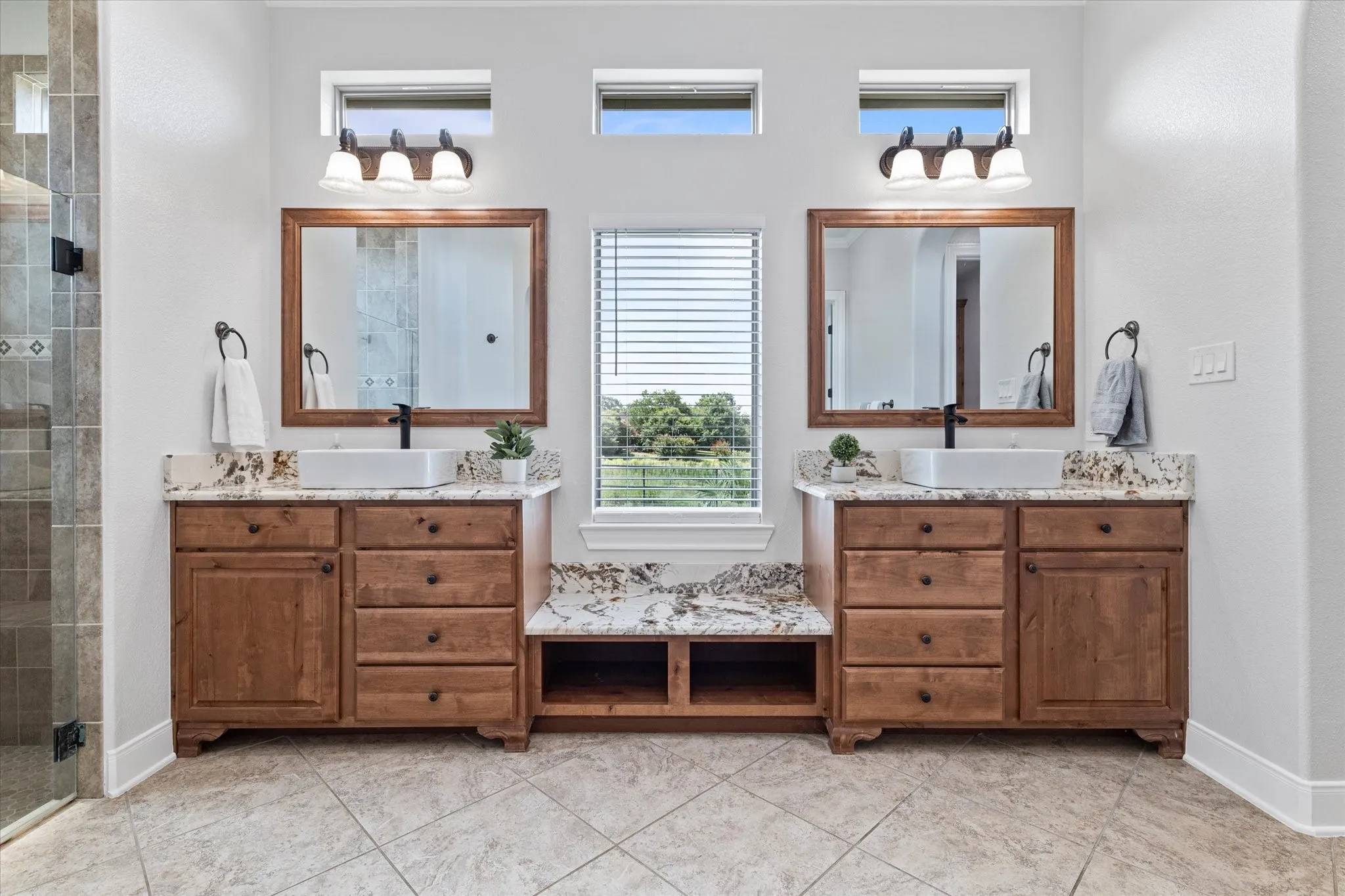 Dual wood-finish vanities with vessel sinks, stone countertops, and dark fixtures