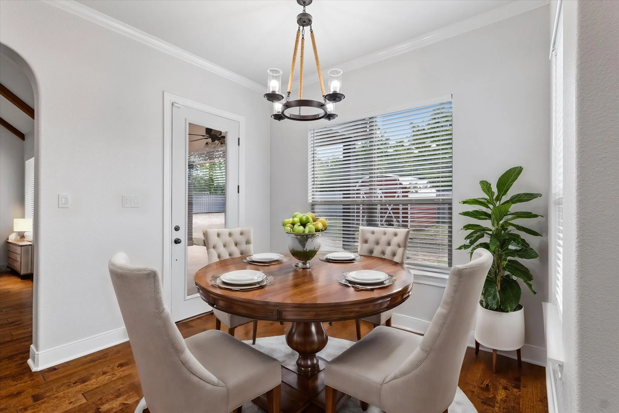 Hardwood-finish flooring, crown molding, arched entry, window with blinds, and a glass-paneled door